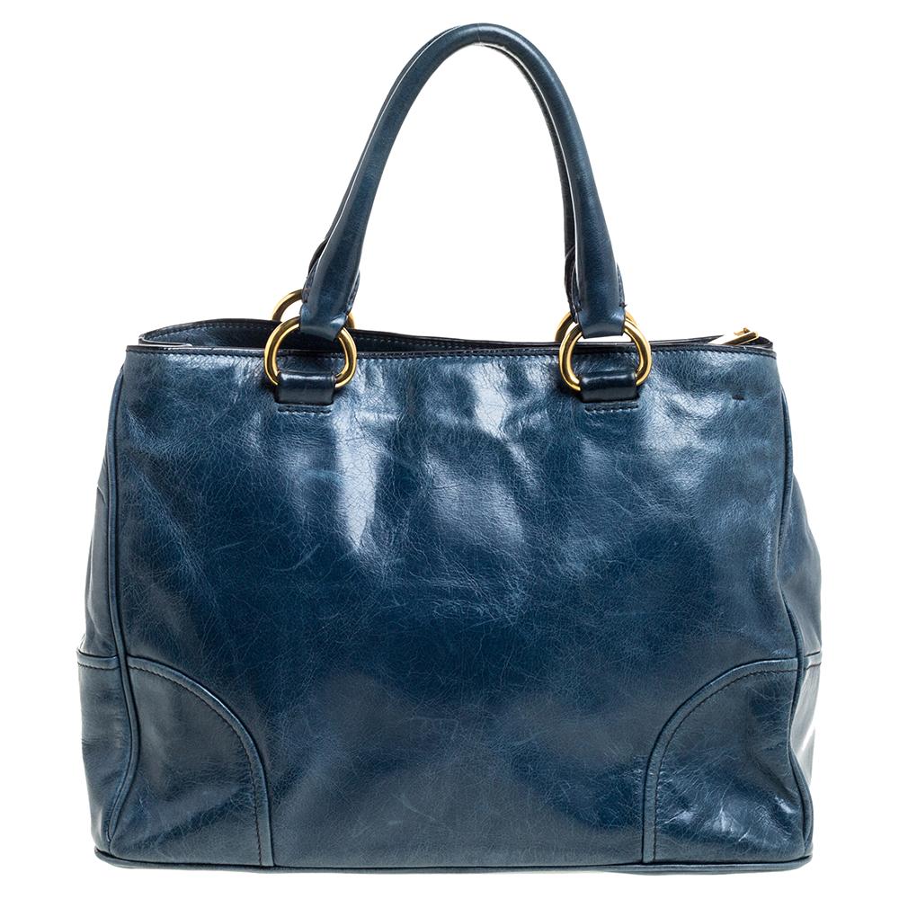 This tote by Prada makes a timeless handbag you will carry for years to come. Crafted from supple leather, the exterior is accented with the brand's accent, rolled handles, a removable shoulder strap, and gold-tone metal feet. The nylon-lined