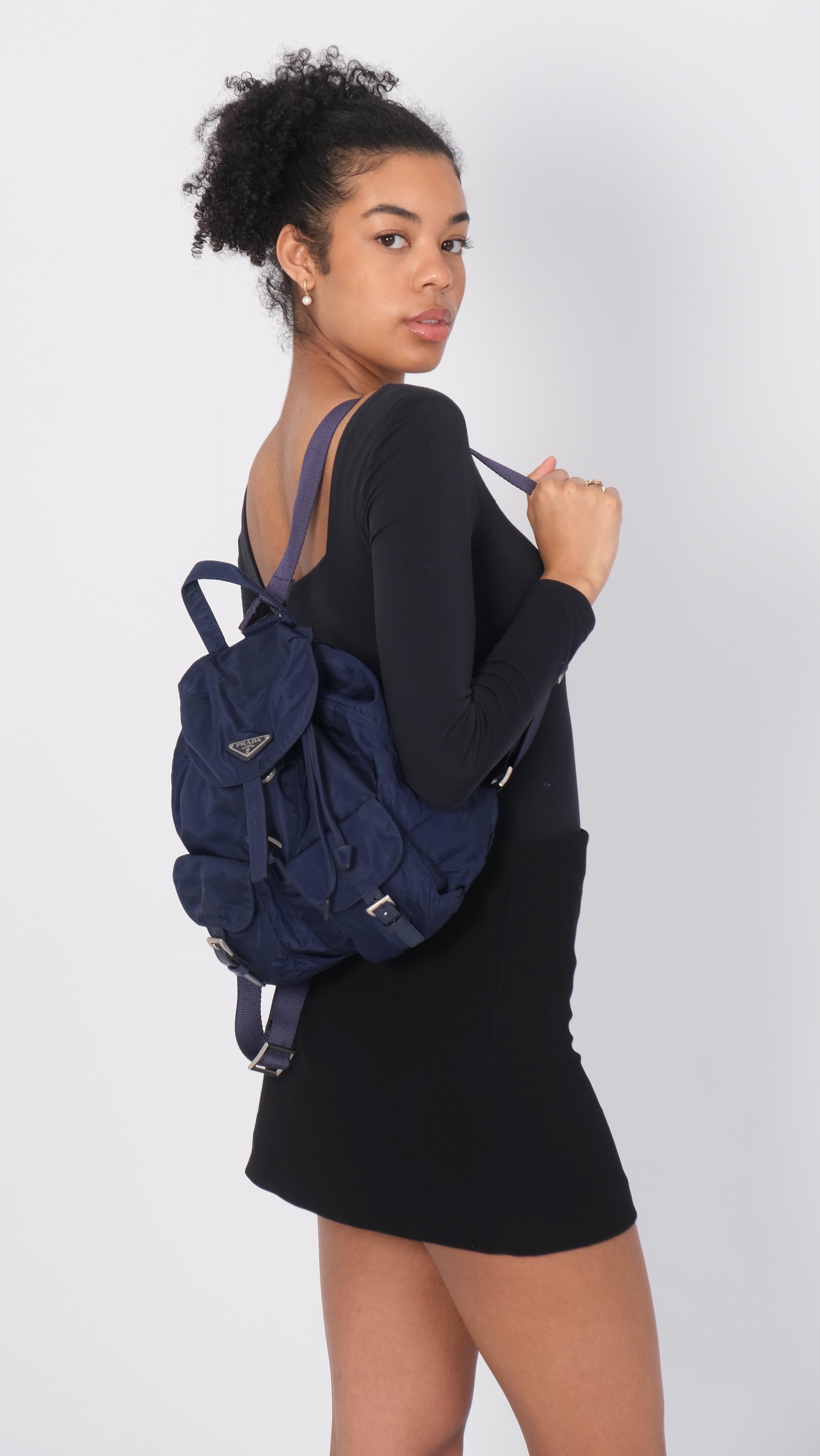 Ce sac à dos est en nylon bleu. Le sac comporte des bretelles réglables en nylon avec des boucles en argent poli, deux poches extérieures à rabat et un rabat croisé sur le dessus avec une sangle et une fermeture à boucle en argent. Ce dernier et la