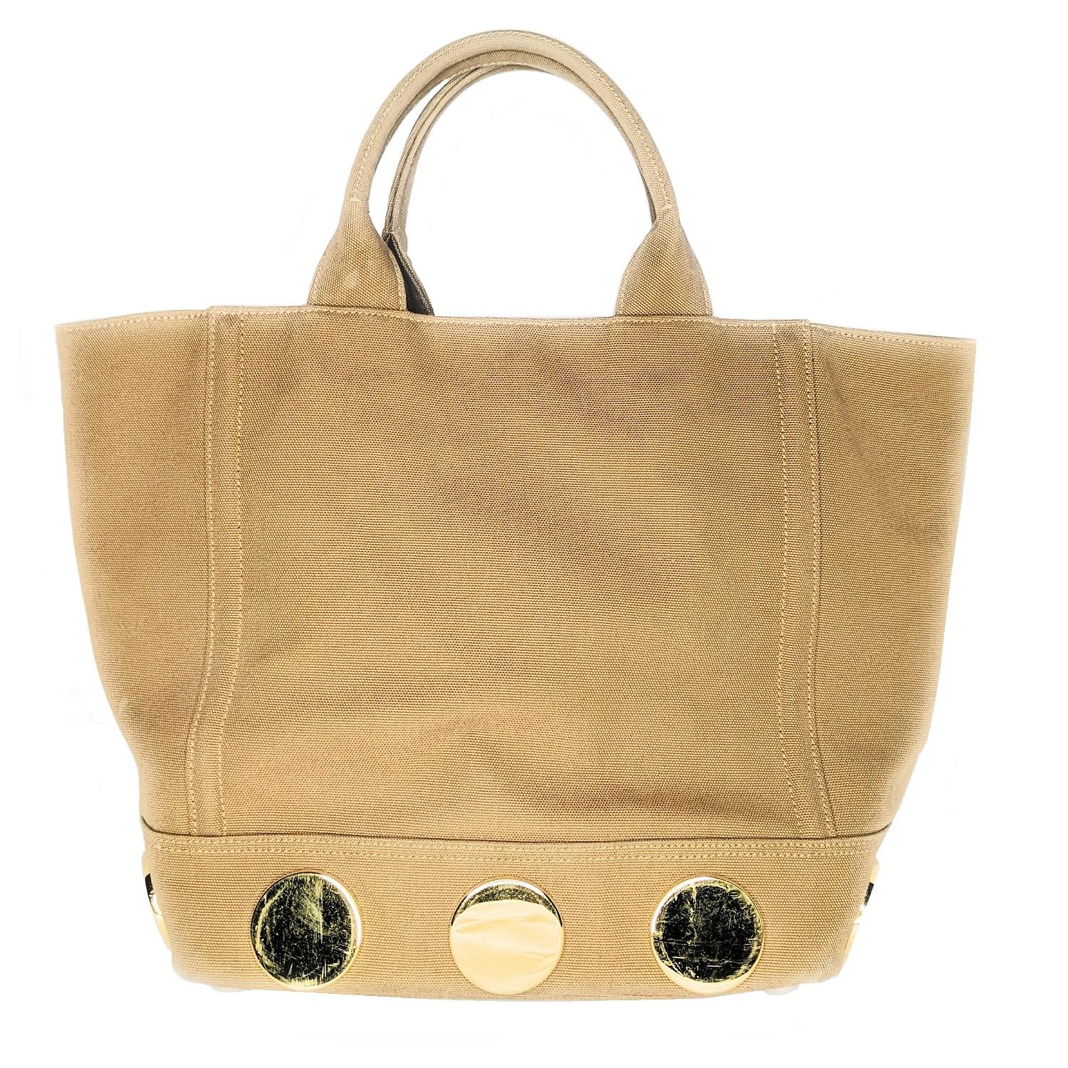 This urban chic tote is made of canvas in a tobacco color with golden hardware and tonal topstitching. The lower part of the bag has nine large gold-tone accented discs making this a bit on the heavy side, weighing in at 2.8 lbs. Open top with