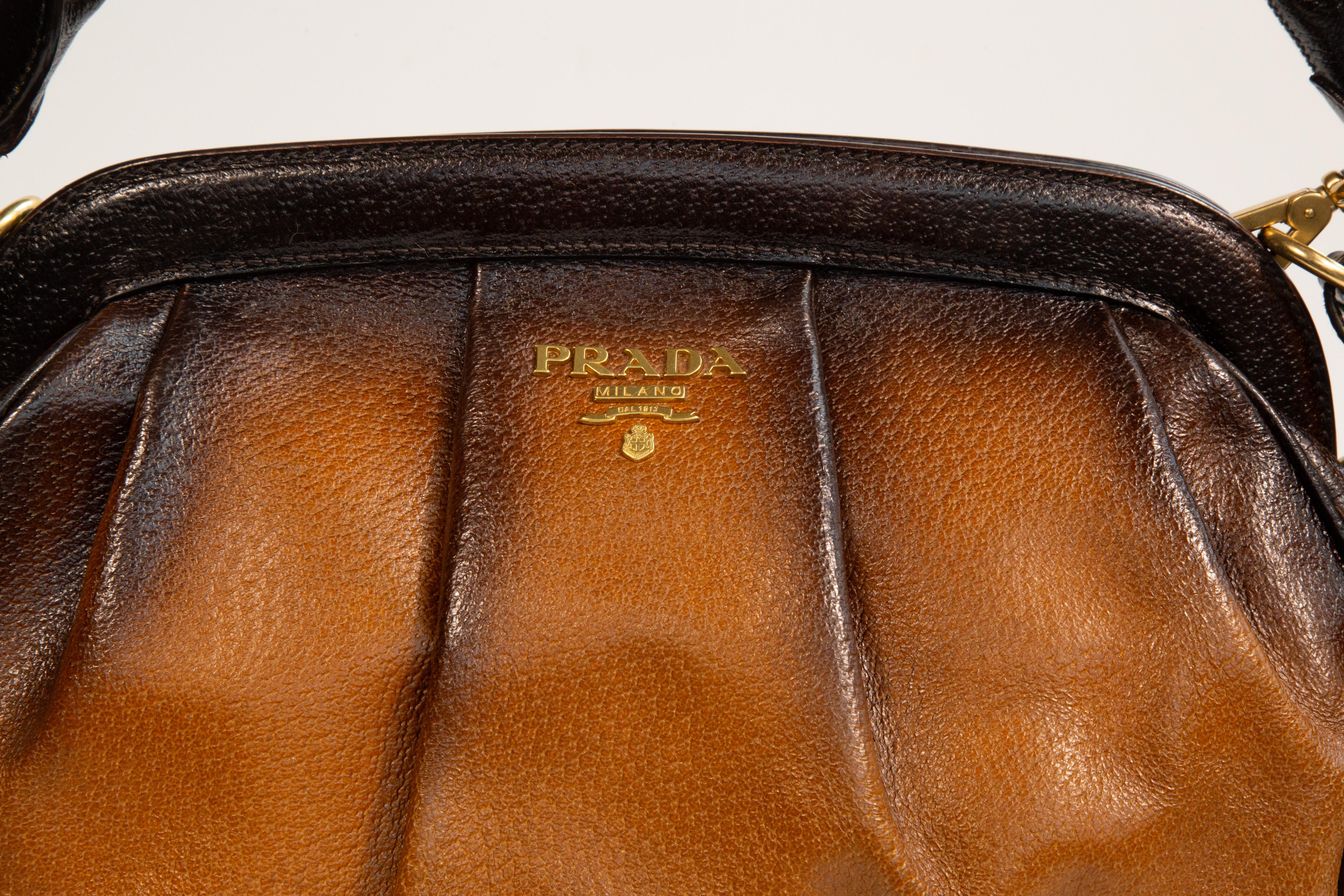 Prada top handle bag/shoulder bag made of leather in different  tones of brown with gold toned hardware. The bag is lined with synthetic fabric with Prada logo. Next to the major compartment, the bag features two side pockets of which one has a