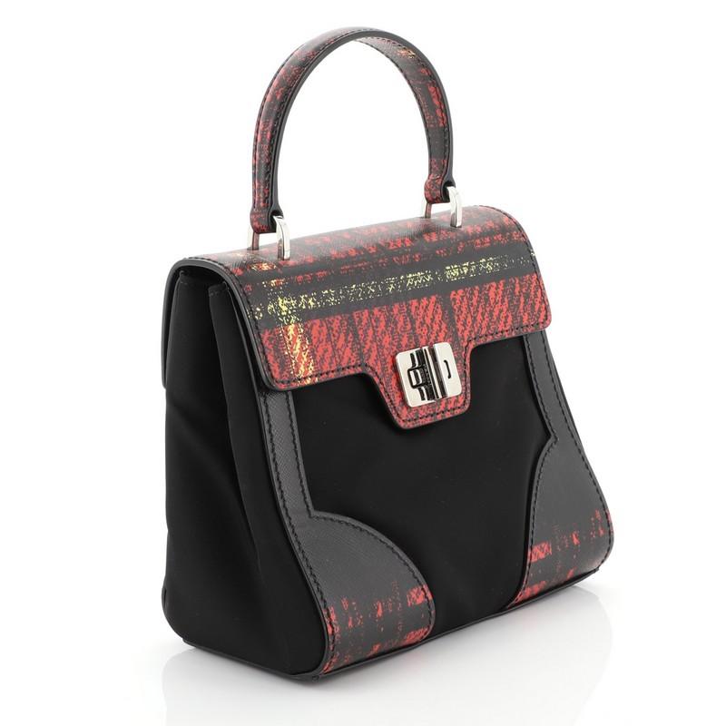 This Prada Turn Lock Top Handle Bag Printed Saffiano Leather with Tessuto Small, crafted from black, red, printed saffiano leather with tessuto, features a leather top handle and silver-tone hardware. Its turn lock closure opens to a black fabric