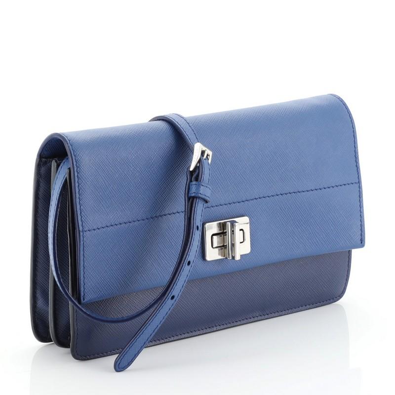 This Prada Turn Lock Wallet Crossbody Saffiano Leather Small, crafted from blue saffiano leather, features an adjustable strap and silver-tone hardware. Its turn-lock closure opens to a blue leather interior with multiple card slots and center zip