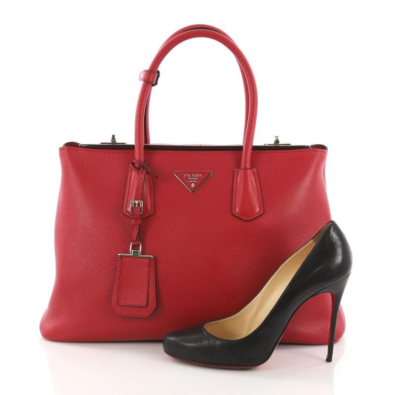 This Prada Turnlock Twin Tote Saffiano Leather Medium, crafted in red saffiano leather, features dual rolled leather handles, protective base studs, and silver-tone hardware. Its dual turn-lock closure opens to a black leather interior divided into