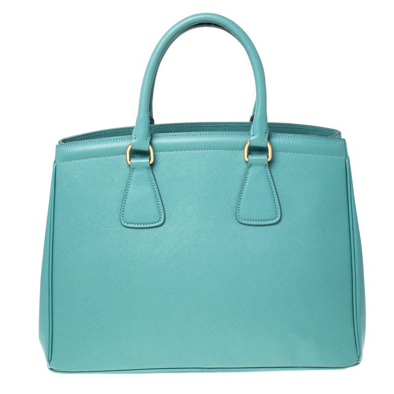 Masterfully created, this Prada tote is a style icon. Designed in a Saffiano Lux leather body, it exudes style and class in equal measures. This delightful turquoise piece is held by two top handles and equipped with a spacious nylon