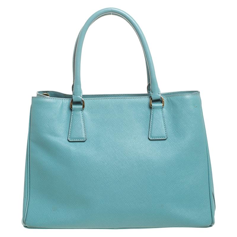 This lovely tote from Prada is crafted from Saffiano Lux leather and comes in a turquoise shade. It flaunts dual round handles, an attached tag, protective metal feet, and a spacious nylon-lined interior. Perfect to complement most of your outfits,