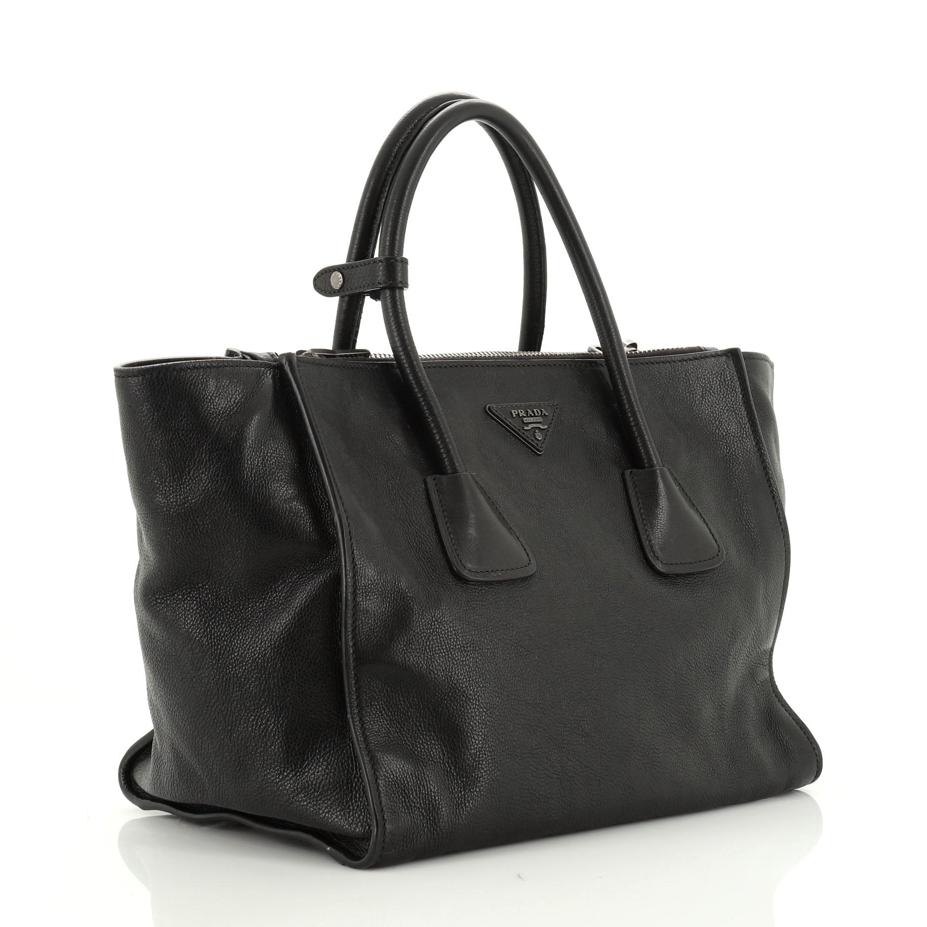 This Prada Twin Pocket Tote Glace Calf Medium, crafted from black glace calf leather, features tall dual rolled top handles, Prada triangle logo, and silver-tone hardware. Its zip closure opens to a gray fabric interior with slip pocket. 

Estimated