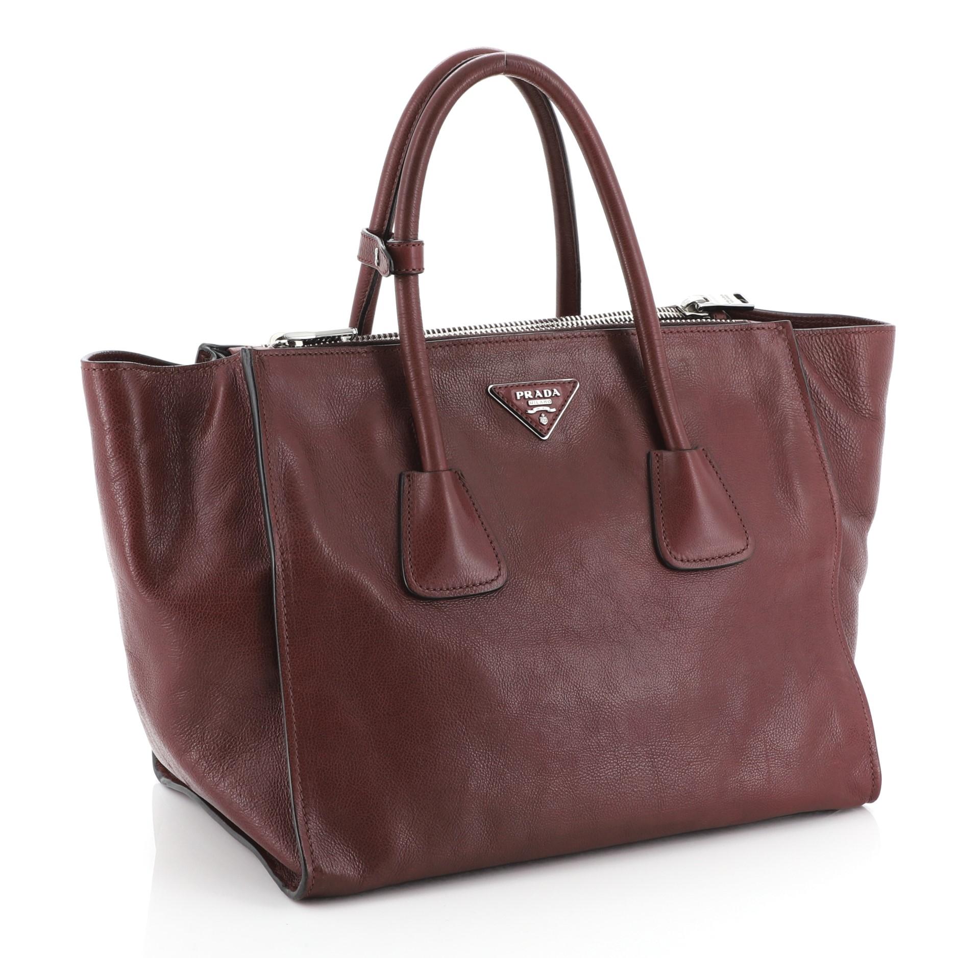 This Prada Twin Pocket Tote Glace Calf Medium, crafted from red glace calf leather, features tall dual rolled top handles, Prada triangle logo, and silver-tone hardware. Its zip closure opens to a black fabric interior with slip pocket. 

Condition: