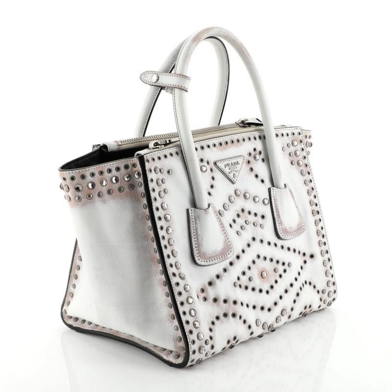 This Prada Twin Pocket Tote Grommet Embellished Leather Small, crafted from white leather, features dual-rolled leather handles, crystal studs and grommet embellishment and silver-tone hardware. It opes to a black leather interior with two side zip