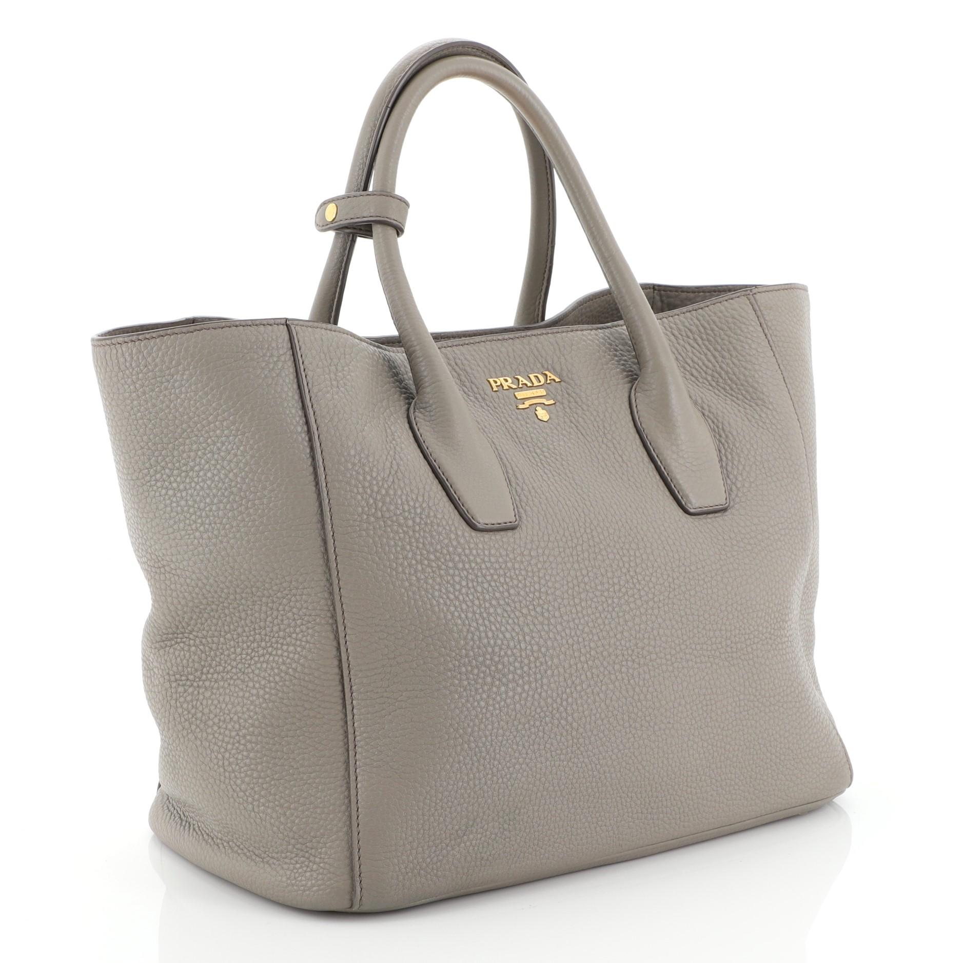 This Prada Twin Shopping Tote Vitello Daino Medium, crafted from neutral vitello daino leather, features dual-rolled handles, side snaps that reveals expanded wings, raised Prada logo, and gold-tone hardware. Its top magnetic snap closure opens to a