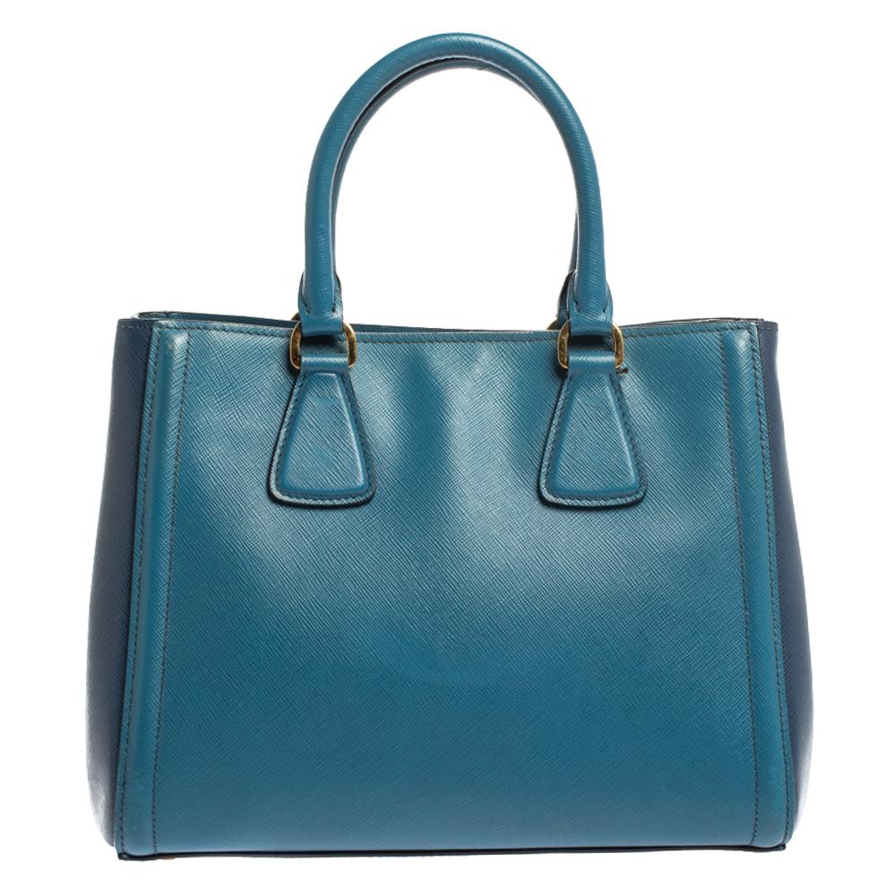 Feminine in shape and grand on design, this small tote by Prada will be a loved addition to your closet. It has been crafted from leather and styled minimally with gold-tone hardware. It comes with two top handles and a nylon-lined interior. The bag