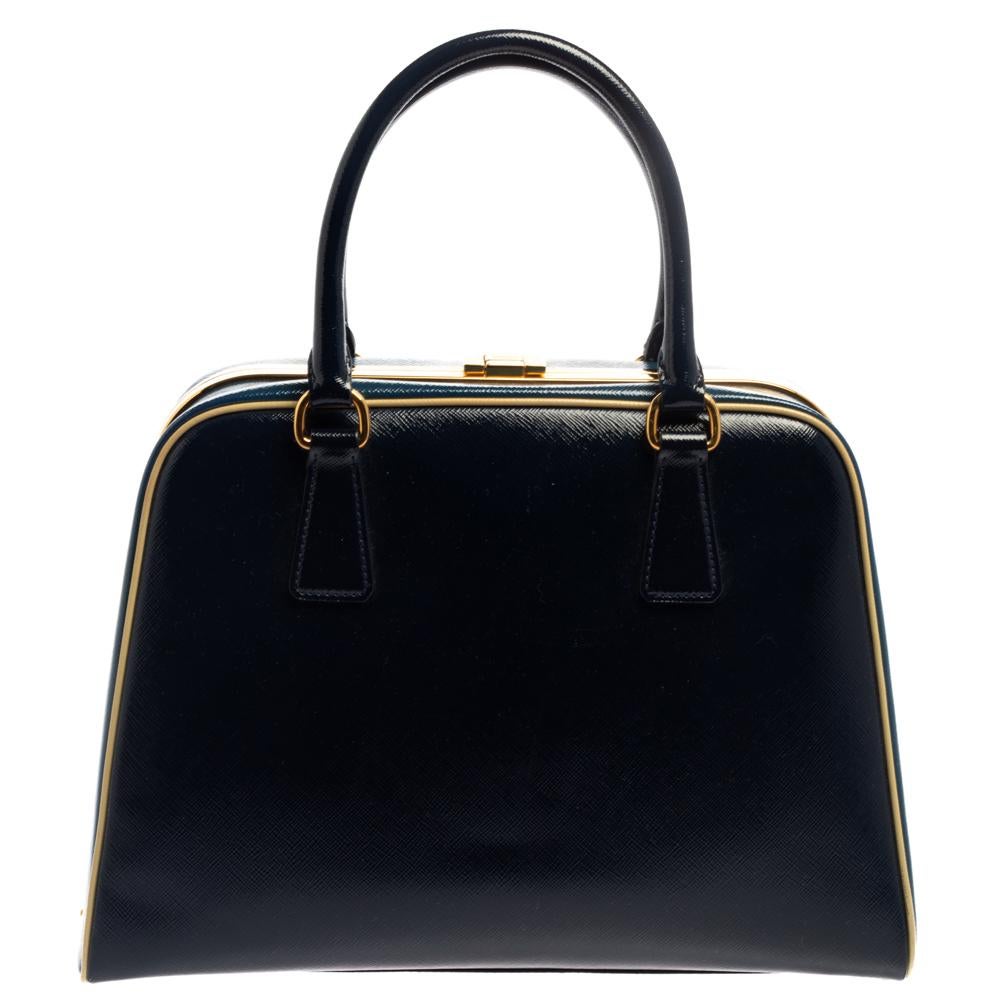 This stunning satchel from Prada is crafted from blue Saffiano Vernice leather and styled with gold-tone hardware in a pyramid frame silhouette. It features dual top handles and a lock closure which opens up to a perfectly sized leather interior