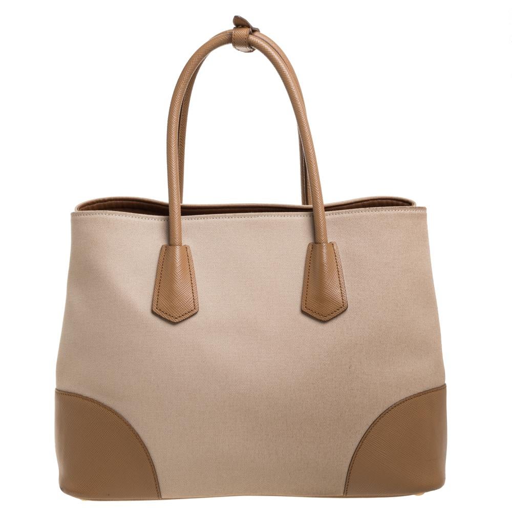 This lovely tote from Prada is crafted from canvas and Saffiano Cuir leather. It flaunts dual top handles, a brand logo on the front, protective metal feet, and a spacious leather-lined interior with enough space to house all your belongings. It is