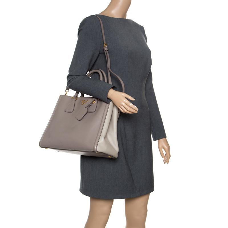 Elegantly crafted exuding a classic finish, this Prada shopper tote is a must-have bag in any fashionista's collection. Made of two-toned taupe Saffiano Lux leather, it features the gold tone Prada logo design at the front along with two flat top
