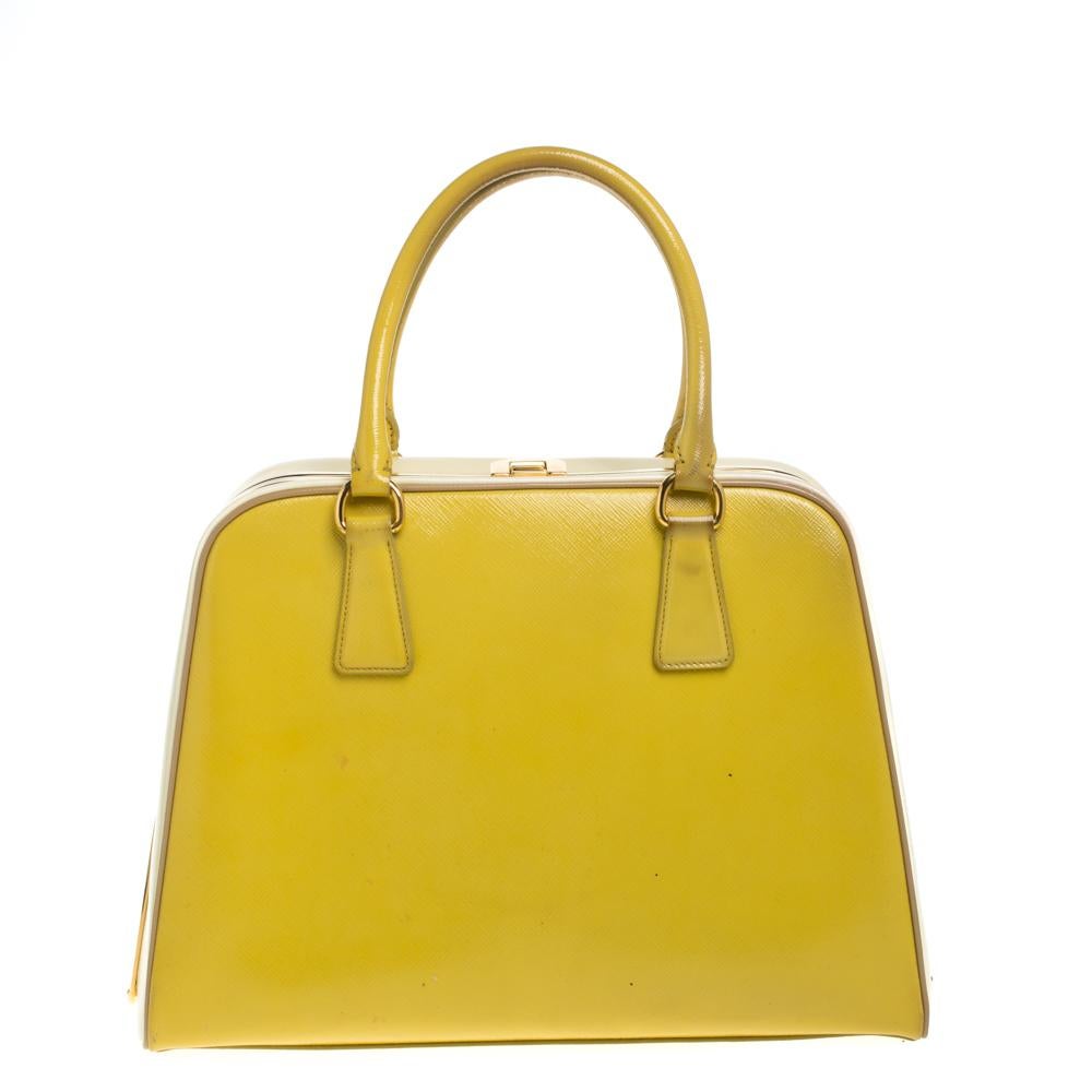 Giving handle bags an elegant update, this Pyramid Frame bag by Prada will be a valuable addition to your closet. It has been crafted from Saffiano Vernice leather and styled with gold-tone hardware. It comes with dual top handles, protective metal