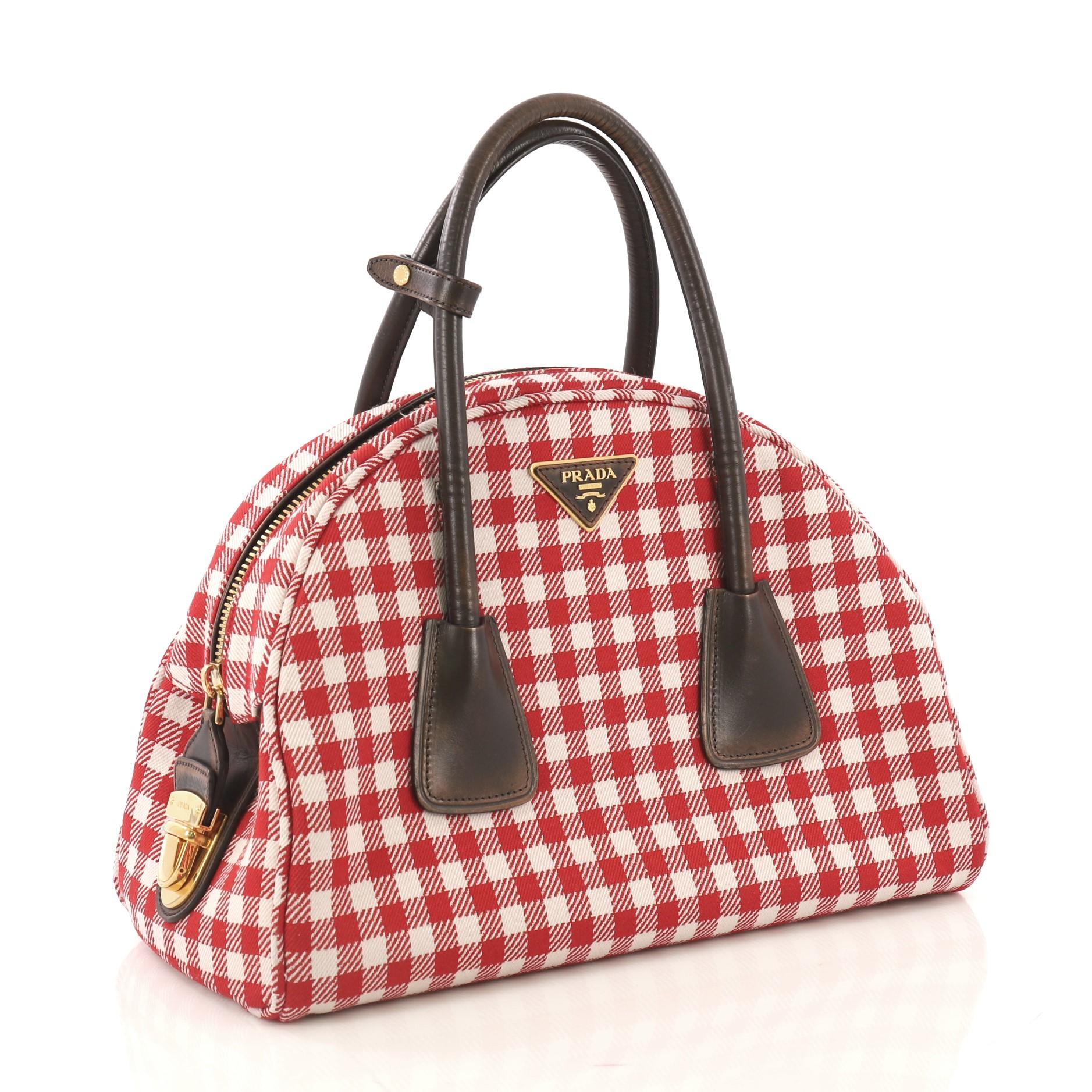 This Prada Vichy Vintage Bowler Bag Jacquard Large, crafted from red and white jacquard, features dual rolled handles, triangular Prada logo at top center, protective base studs and aged gold-tone hardware. Its zip closure with push-lock opens to a