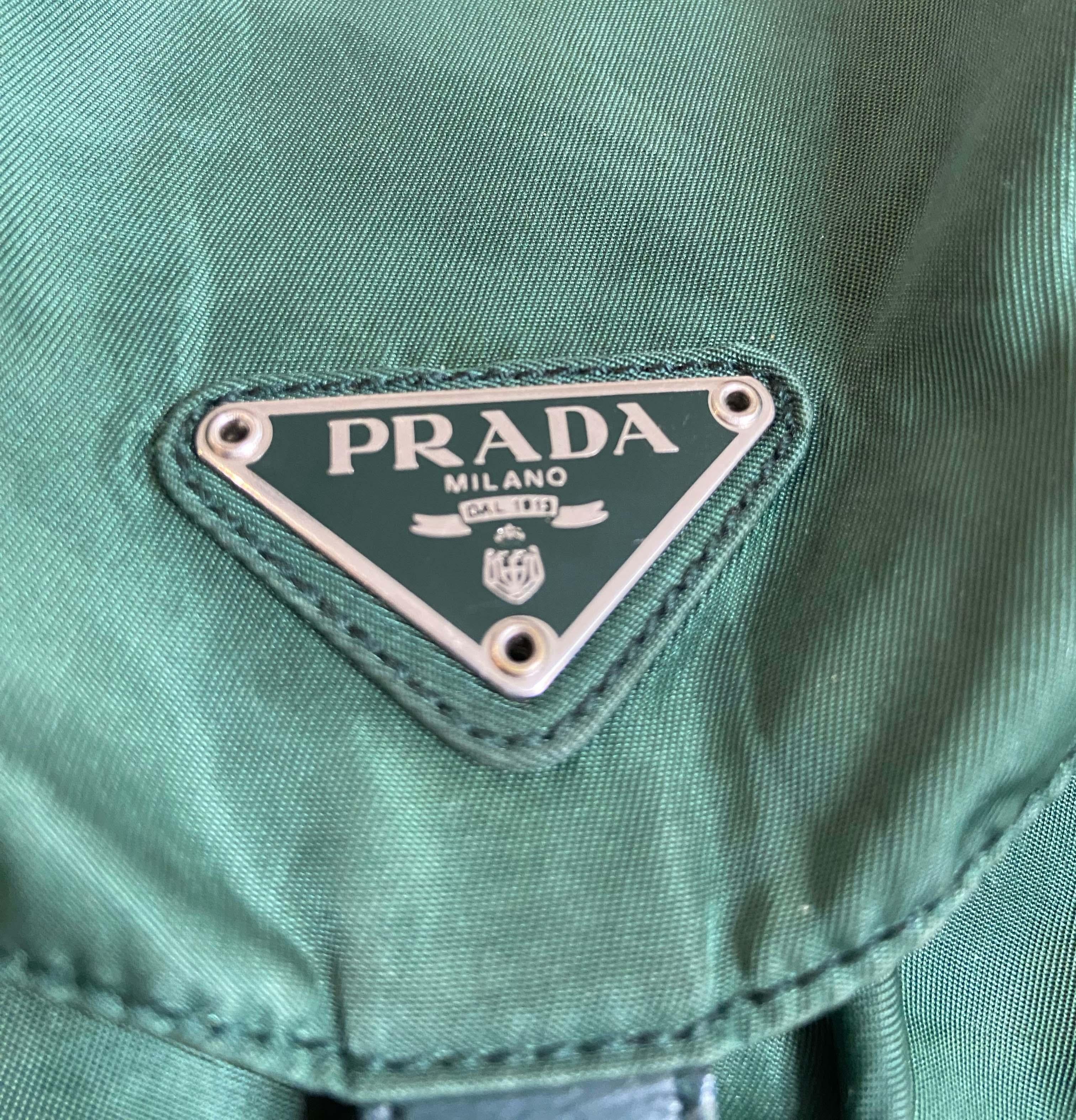 Prada vintage 1990's green nylon backpack. Features green canvas, leather details and silver buckles. Adjustable woven nylon straps, enamel metal triangle logo on the front flap, two small zip up pockets at the front and one inner zip pocket.