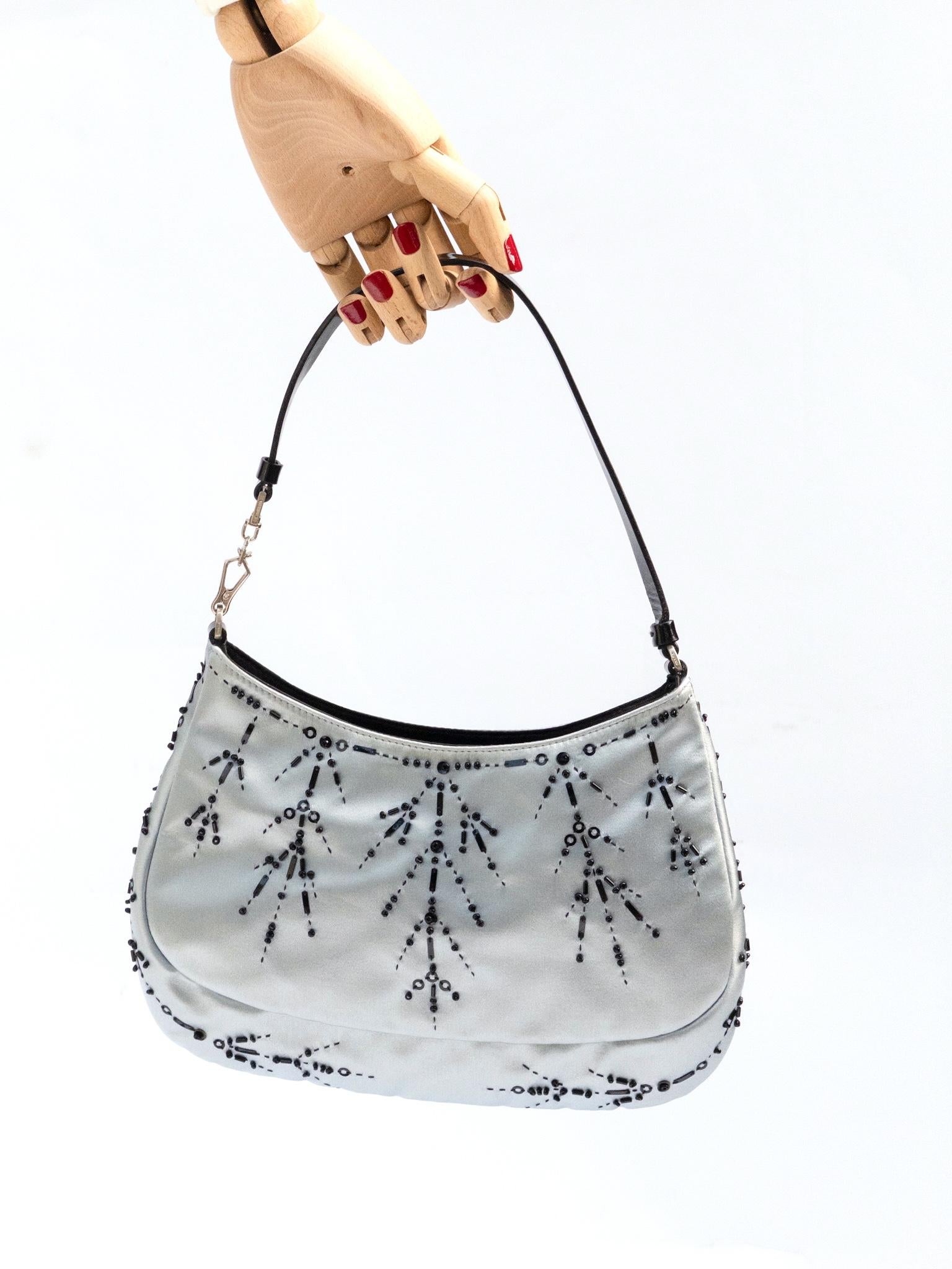 Diese Tasche ist Pradas verspielte Version des ikonischen Cleo-Stils. Sie ist aus schimmerndem, eisblauem Seidensatin gefertigt und von Hand mit tiefschwarzen Perlen verziert, die in zarten, symmetrischen Stößen angeordnet sind. Die schlanke,