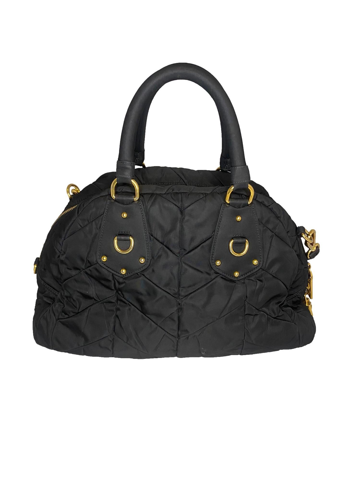 Black quilted Tessuto bowling bag by Prada. Fabric quilted outer with leather detail. Gold coloured hardware. Double rolled handles attached with gold D rings. Vintage signature Prada Milano logo in gold on front side. Chunky top zip closure with
