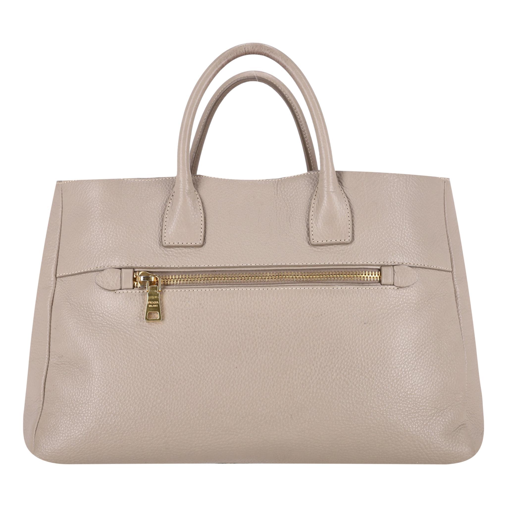 Prada Vitello Daino Leather Handbag

Beige bag crafted from leather with signature 'Prada Milano' logo in gold.

Featuring zipped pocket to the front and rear.

Dual top handle and top snap closure leading to logo lined interior with open and zipped