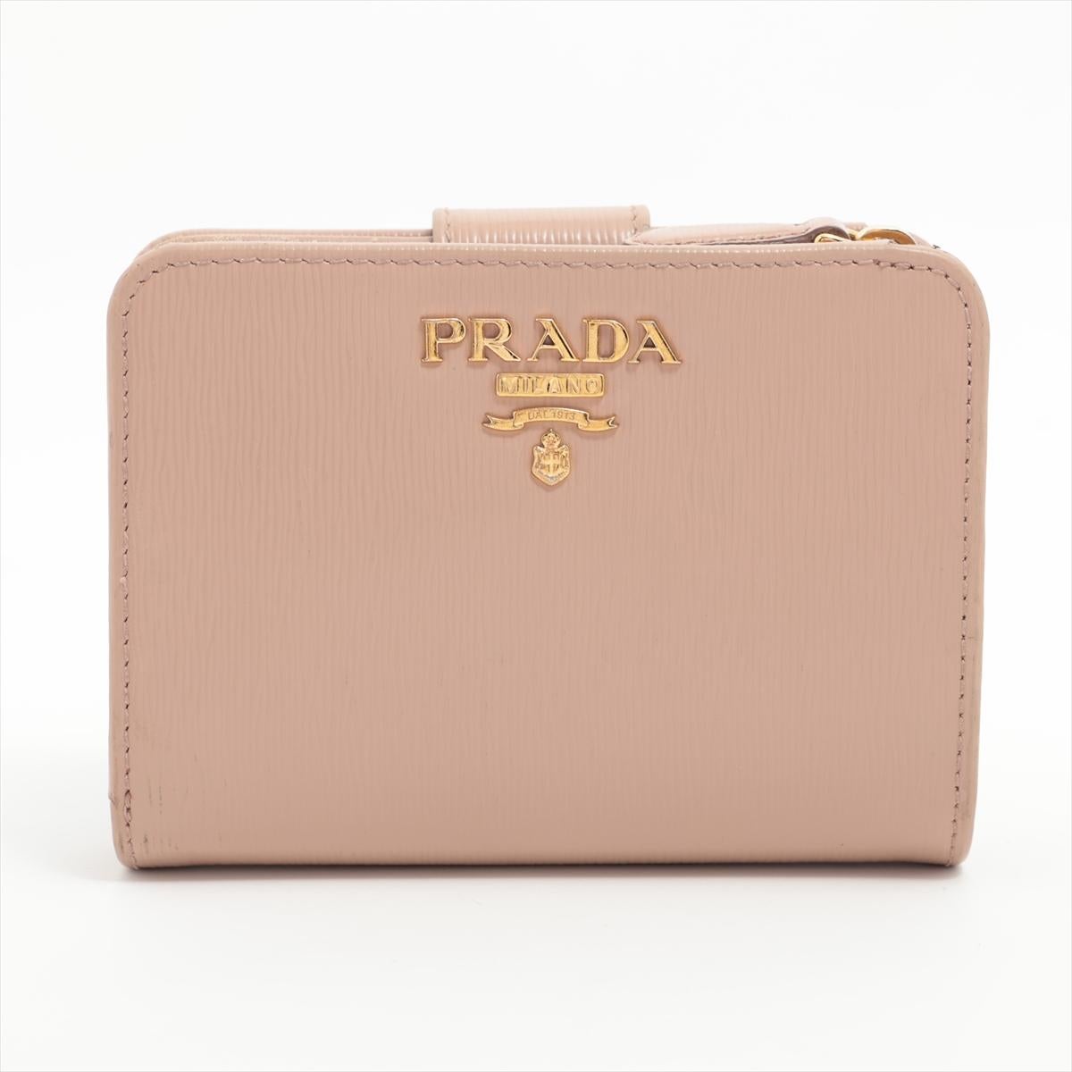 The Prada Vitello Leather Compact Wallet in Beige is a testament to the brand's commitment to modern elegance and functionality. Crafted from luxurious Vitello leather, renowned for its smooth texture and durability, the compact wallet effortlessly