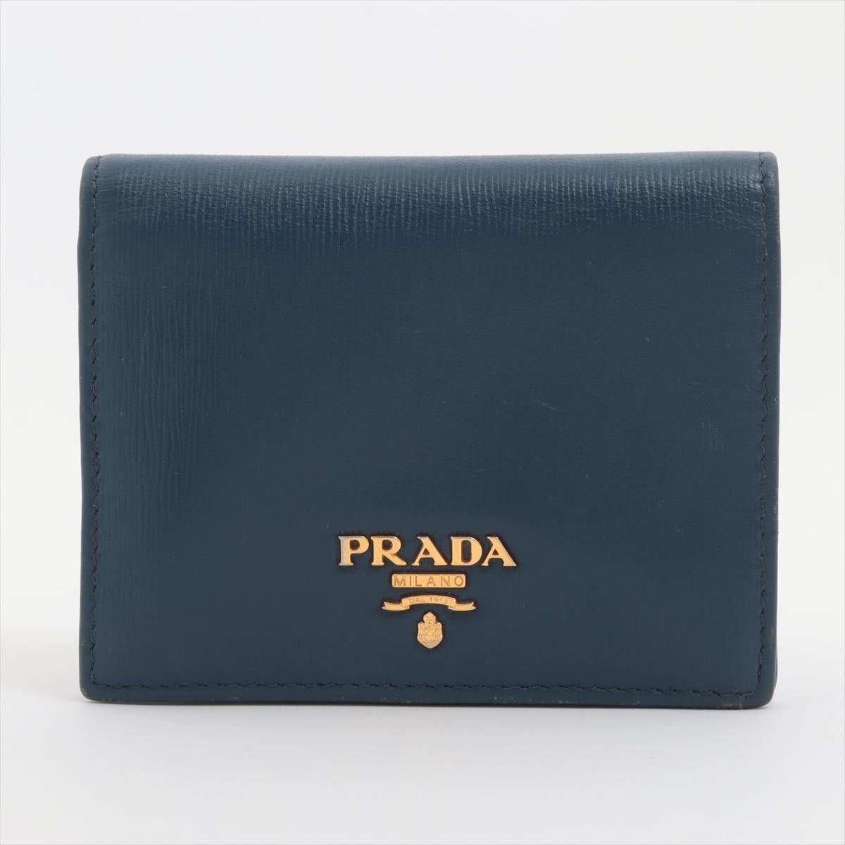 The Prada Vitello Move Leather Compact Wallet in Blue is a chic and versatile accessory that effortlessly combines functionality with luxury. Crafted from Prada's signature Vitello Move leather, the wallet boasts a smooth texture and a rich blue
