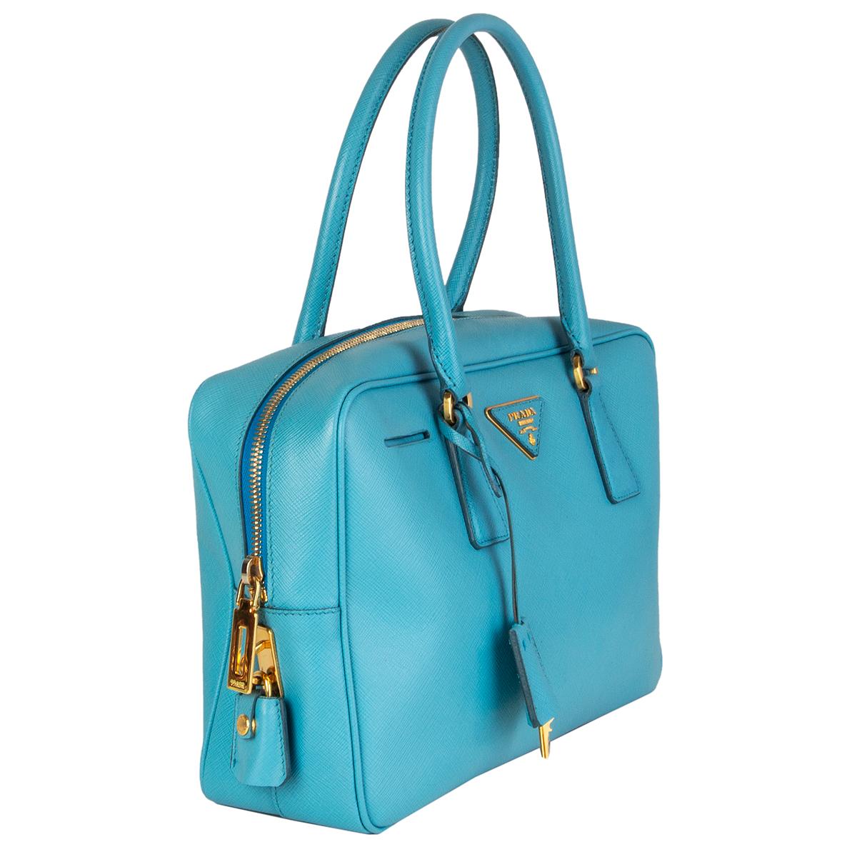 Prada 'Scarlatto BL0095' bag in voyage (light blue) Saffiano Lux leather featuring gold-tone hardware. Opens with a zipper on top and is lined in blue monogram canvas with one zipper pocket against the back. Has been carried with shadow