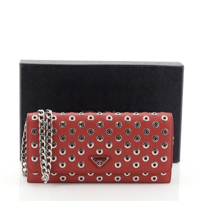 This Prada Wallet on Chain Grommet Embellished Leather, crafted from red saffiano leather, features chain-link shoulder strap, raised Prada logo, grommet embellishment and silver-tone hardware. Its snap closure opens to a black leather interior with