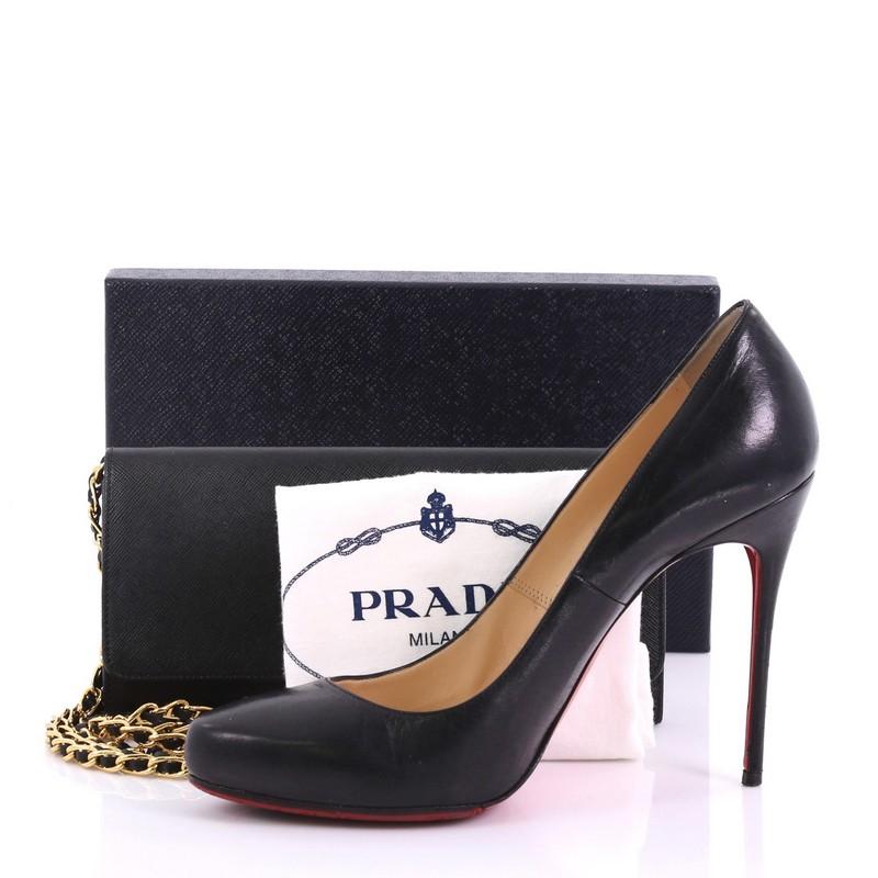 This Prada Wallet on Chain Saffiano Leather, crafted from black saffiano leather, features an adjustable gold chain shoulder strap entwined with leather, raised Prada logo, and gold-tone hardware. The bag’s hidden double snap closure opens to a
