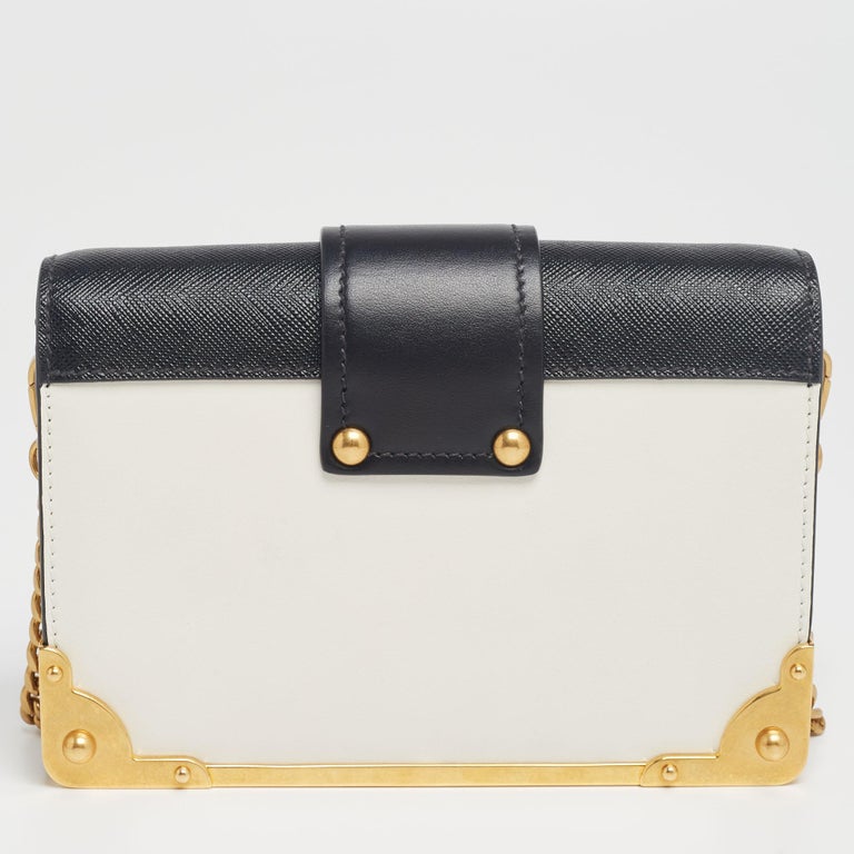 Inspired by valuable books from ancient times, the Cahier by Prada is a best-seller. This bag is crafted using black and white leather and gold-tone hardware. The strap closure with the brand logo opens to a leather-lined interior with enough space
