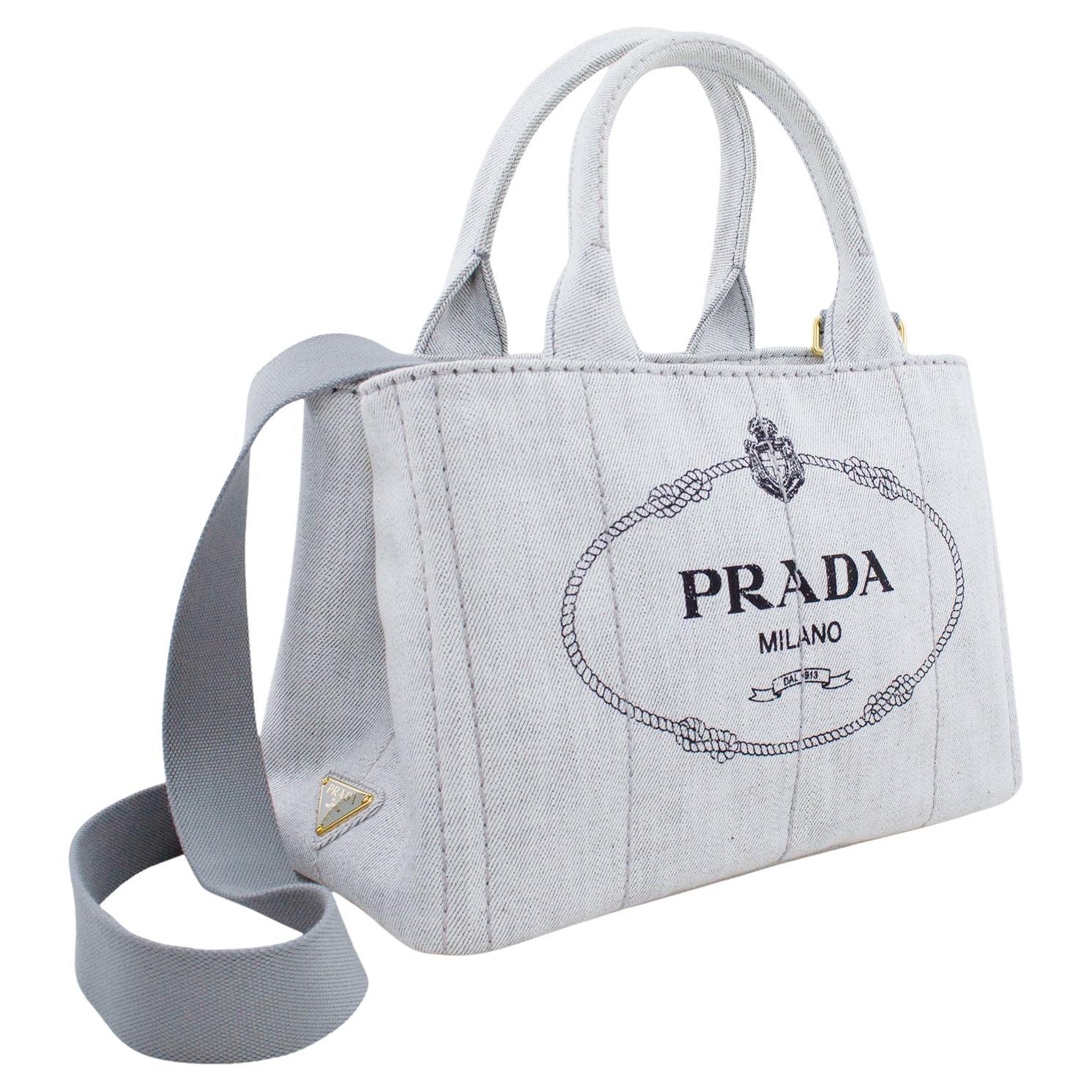 This current Prada tote bag was inspired by vintage gardener's bags. White denim printed with a silk-screen logo and embellished with brass-finish hardware, it offers three practical internal pockets and a detachable shoulder strap. Excellent