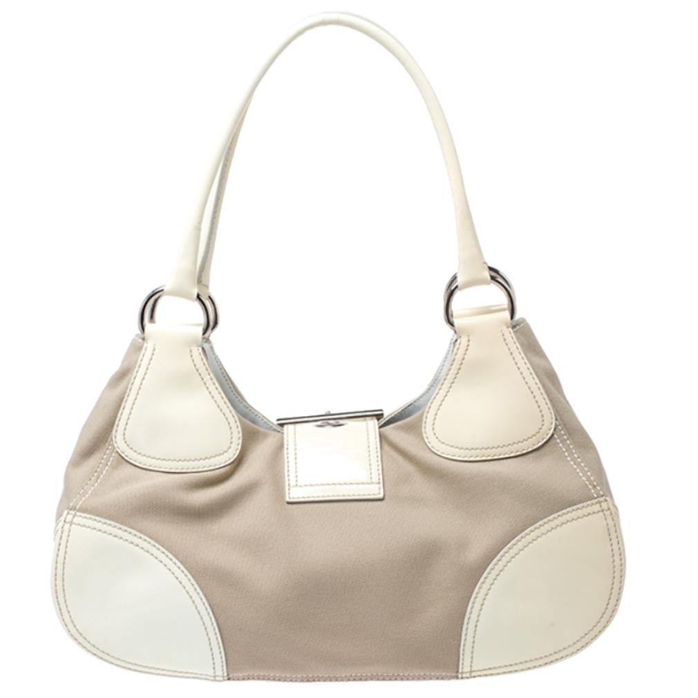 This white Prada bag is effortlessly stylish. Crafted from leather and canvas, it is held by dual handles, comes with buckle closure, fabric-lined interior with a zip pocket and enough space to carry your essentials. It is finished with silver-tone