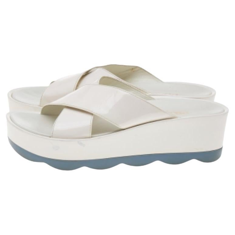 Le confort et le style sont réunis avec ces diapositives plates de la maison Prada ! Elles sont confectionnées en cuir verni blanc et dotées d'une bride croisée sur le dessus. Ils sont surélevés sur des plates-formes. Ces diapositives sont un cadeau