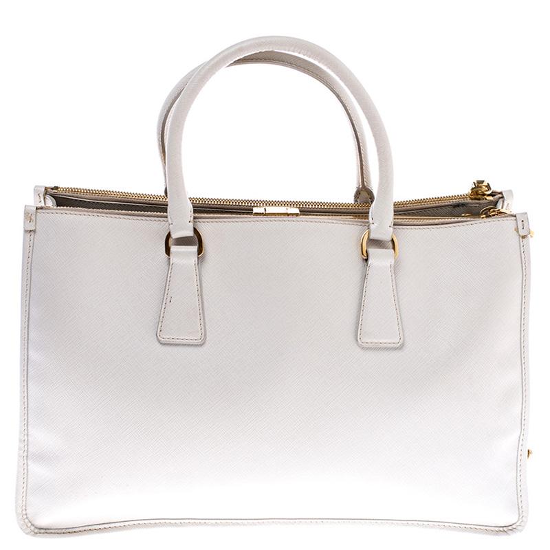 This structured handle bag by Prada is crafted from fine and exclusive Saffiano lux leather. The white-colored bag features double rolled leather handles and a kiss-lock frame with a compartment in the middle to keep your valuables safe. It also