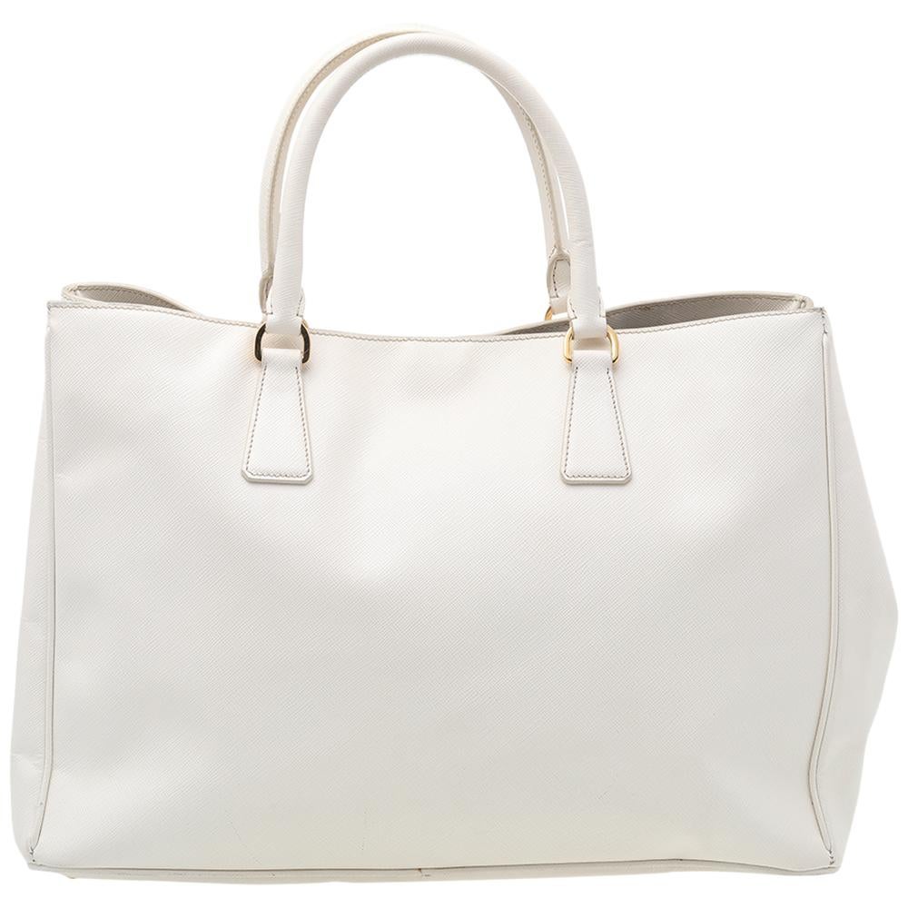 Loved for its classic appeal and functional design, Galleria is one of the most iconic and popular bags from the house of Prada. This white beauty is crafted from Saffiano Lux leather and is equipped with two top handles, the triangular brand logo