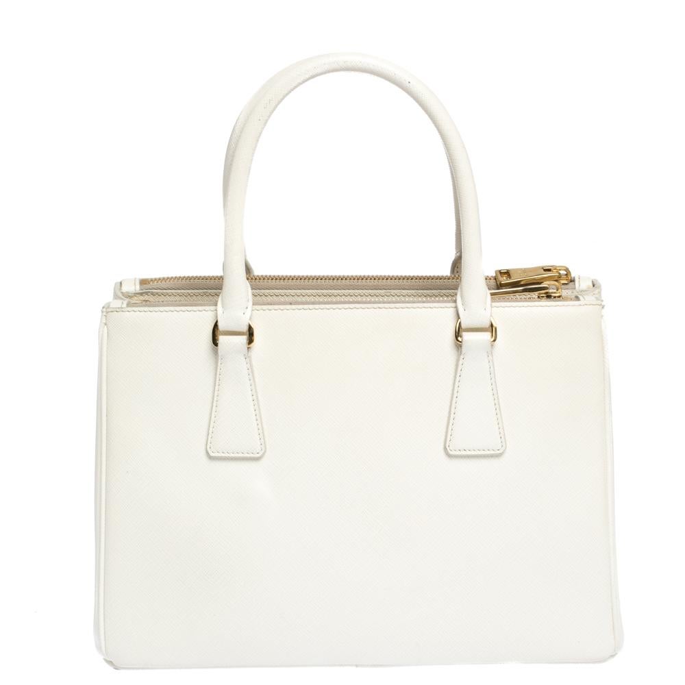 Feminine in shape and grand in design, this Double Zip tote by Prada will be a loved addition to your closet. It has been crafted from Saffiano Lux leather and styled minimally with gold-tone hardware. It comes with two top handles, two zip