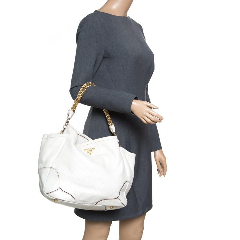 This shimmering white chain hobo is yet another Prada masterpiece. Crafted from white deerskin leather with gold-tone hardware, It is accented with a gold-tone Prada logo at the front, and chain link and leather shoulder strap. The interior is lined