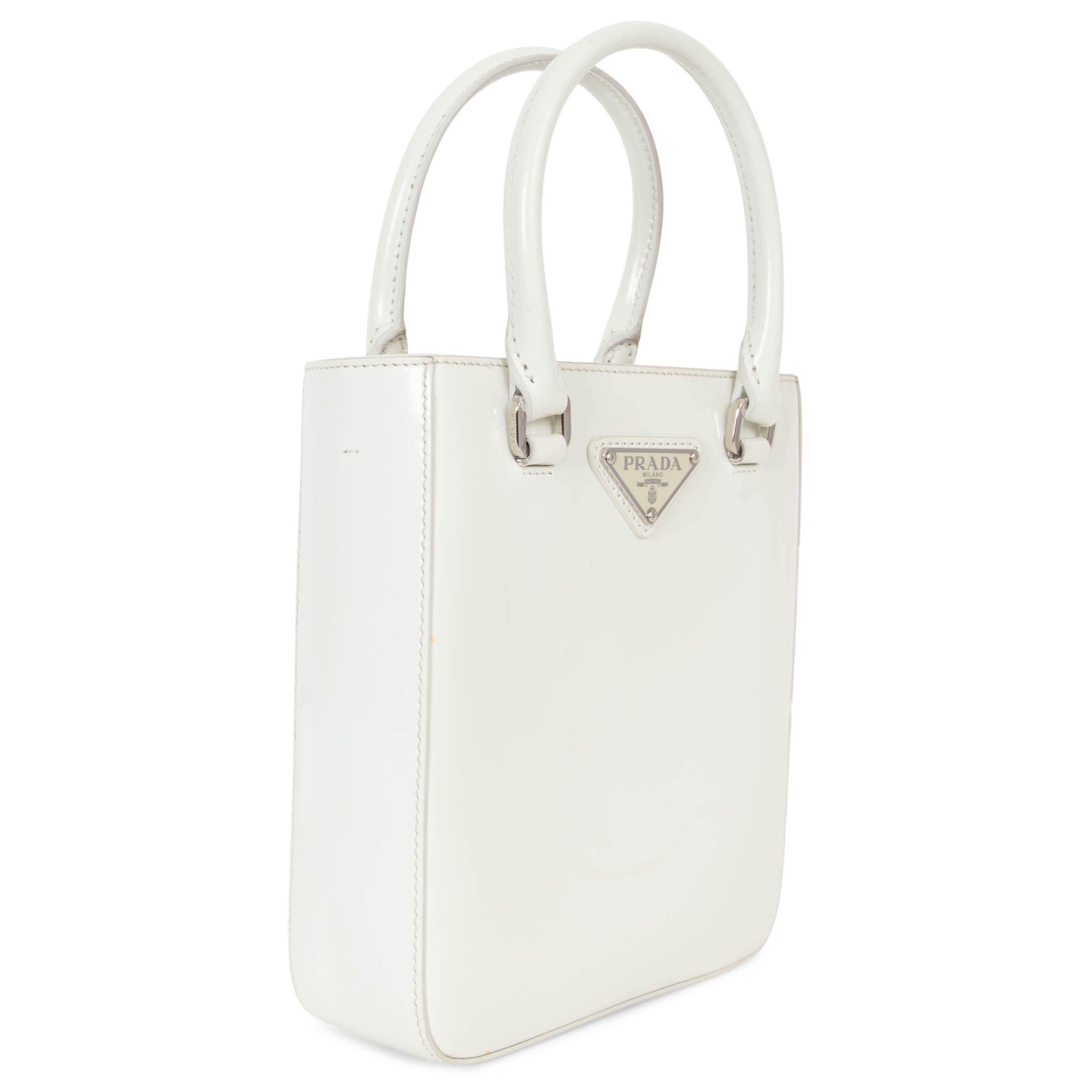 This 100% authentic Prada Small Tote bag in Bianco cream brushed Spazzolato leather is a sophisticated blend of timeless elegance and modern versatility. Adorned with the signature enamelled logo triangle and silver-tone hardware, it offers a