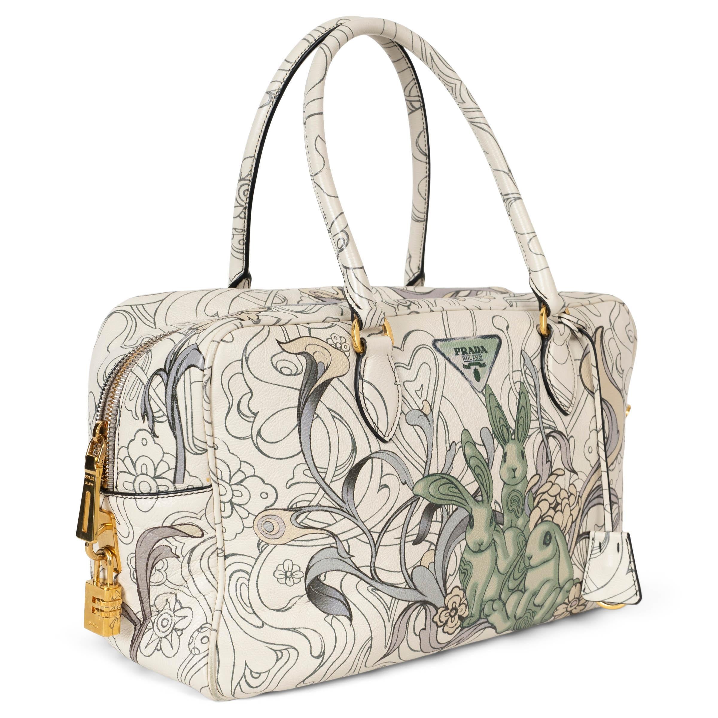 This 100% authentic Prada x James Jean Bauletto bag is a stunning blend of art and luxury. Crafted from ivory, grey, and green glacé calfskin, it features James Jean’s whimsical lop bunny print, making it a true collector's piece. The bag is