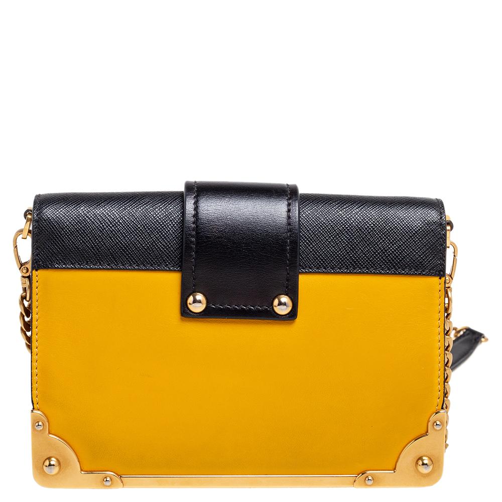 Inspired by valuable books from ancient times, the Cahier by Prada is a best-seller. This shoulder bag is crafted in Italy with black and yellow leather. It features gold-tone trims that add a touch of contrast. The strap closure with the brand logo