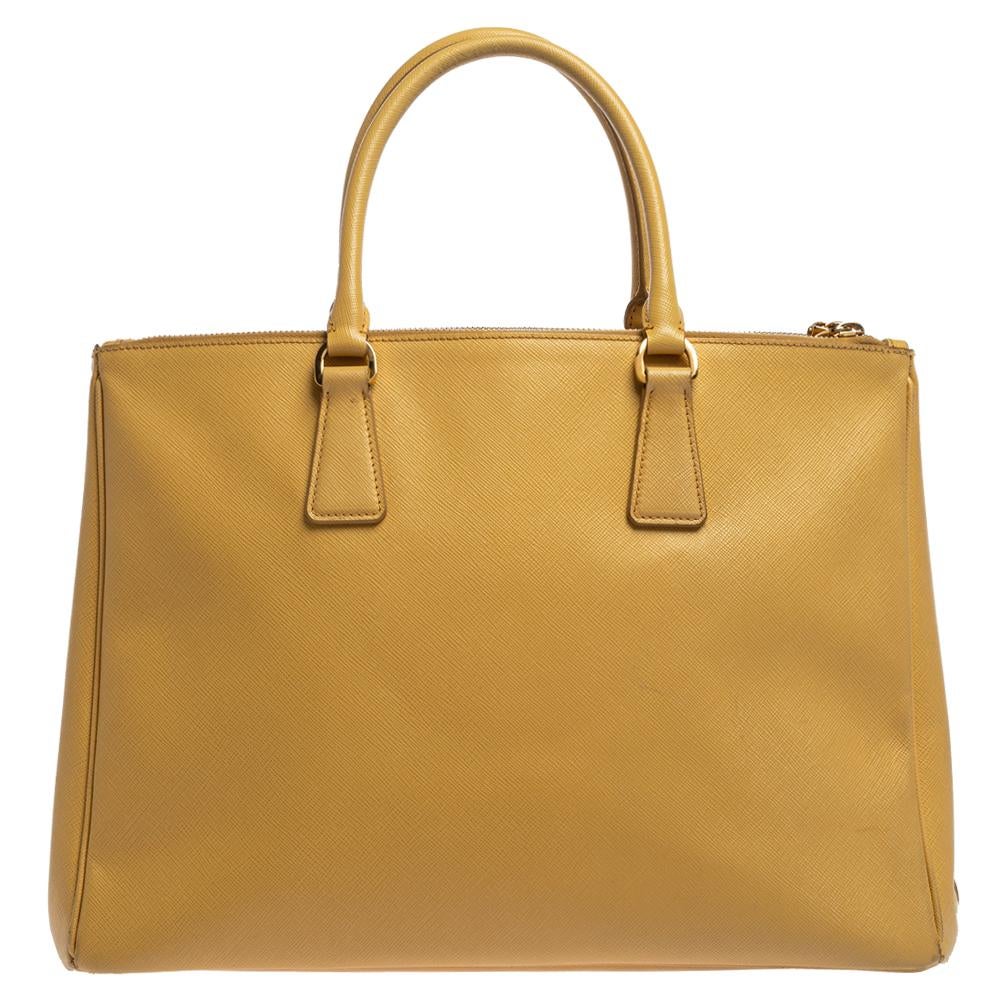 Feminine in shape and grand in design, this Double Zip tote by Prada will be a loved addition to your closet. It has been crafted from Saffiano Lux leather and styled minimally with gold-tone hardware. It comes with two top handles, two zip