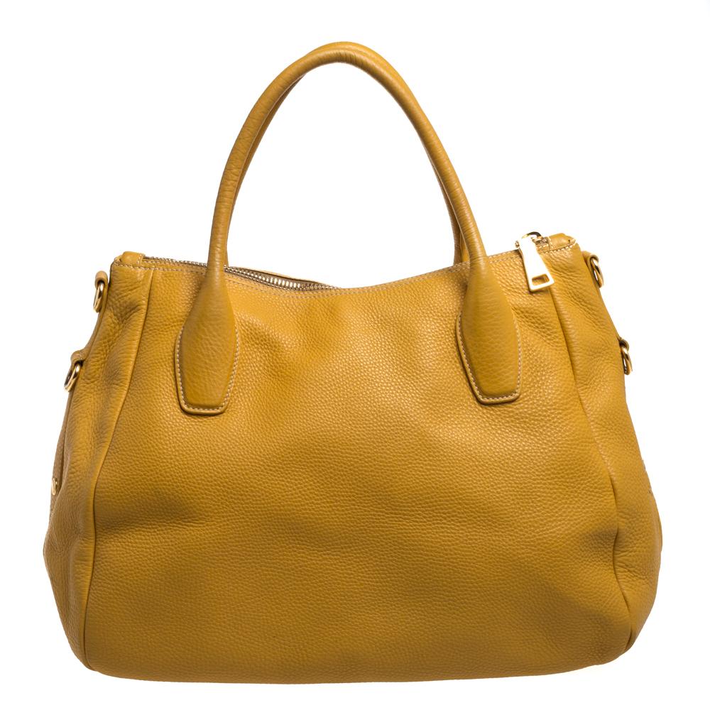 This Prada Sacca 2 Manici tote is made of Vitello Daino leather. It features rolled top handles and gold-tone hardware. A recognizable Prada logo sits at the front. The interior is lined with durable nylon and comprises a slip pocket and enough