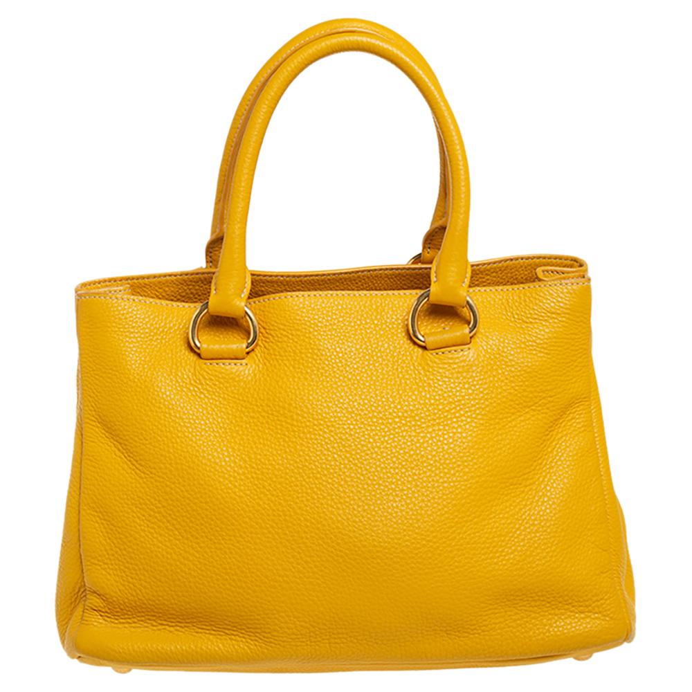 This lovely tote from Prada is crafted from leather and features a yellow shade. It flaunts dual handles, an attached tag, protective metal feet, and a spacious interior. Perfect to complement most of your outfits, this bag is worth every cent and