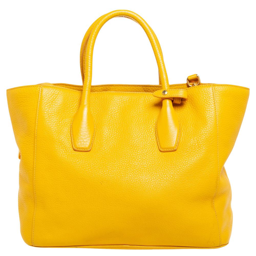 Loved for their classic appeal and functional design, tote bags are one of the most iconic and popular bags from the house of Prada. This beauty in yellow is crafted from Vitello Daino leather and is equipped with two top handles and the brand logo