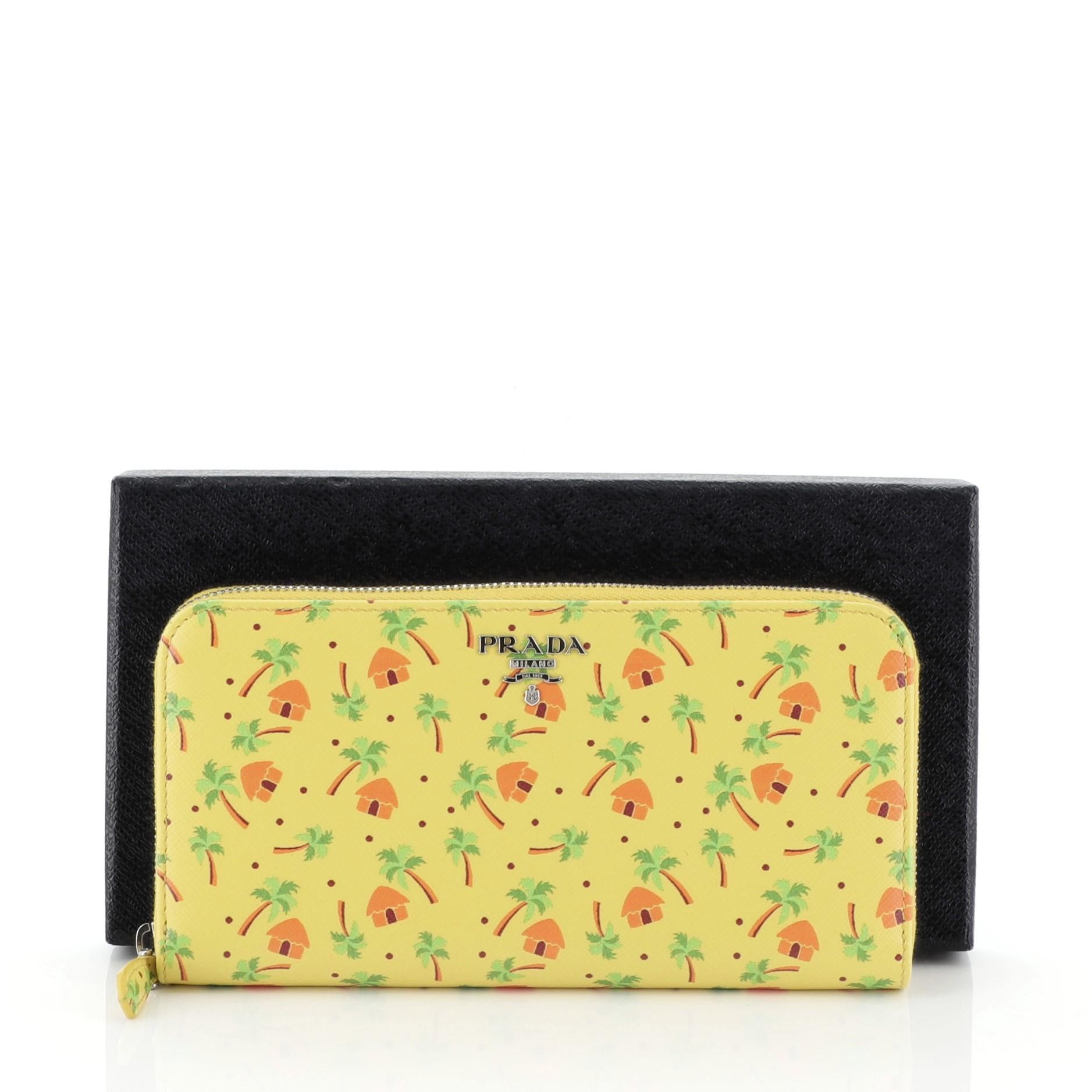 This Prada Zip Around Wallet Printed Saffiano Long, crafted from yellow printed saffiano leather, features silver-tone hardware. Its zip closure opens to a yellow leather interior with multiple card slots and zip pocket. 

Estimated Retail Price: