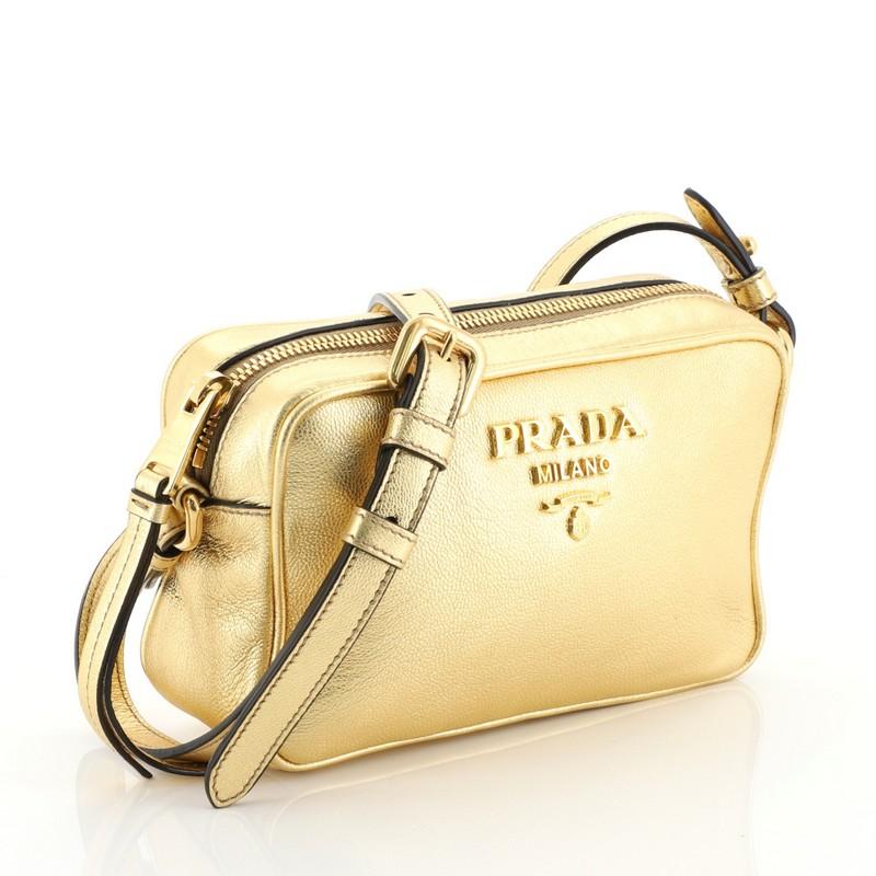 This Prada Zip Crossbody Bag Vitello Daino Mini, crafted in metallic gold leather, features an adjustable leather strap, signature Prada logo, and gold-tone hardware. Its zip closure opens to a black fabric interior with slip pockets. These are