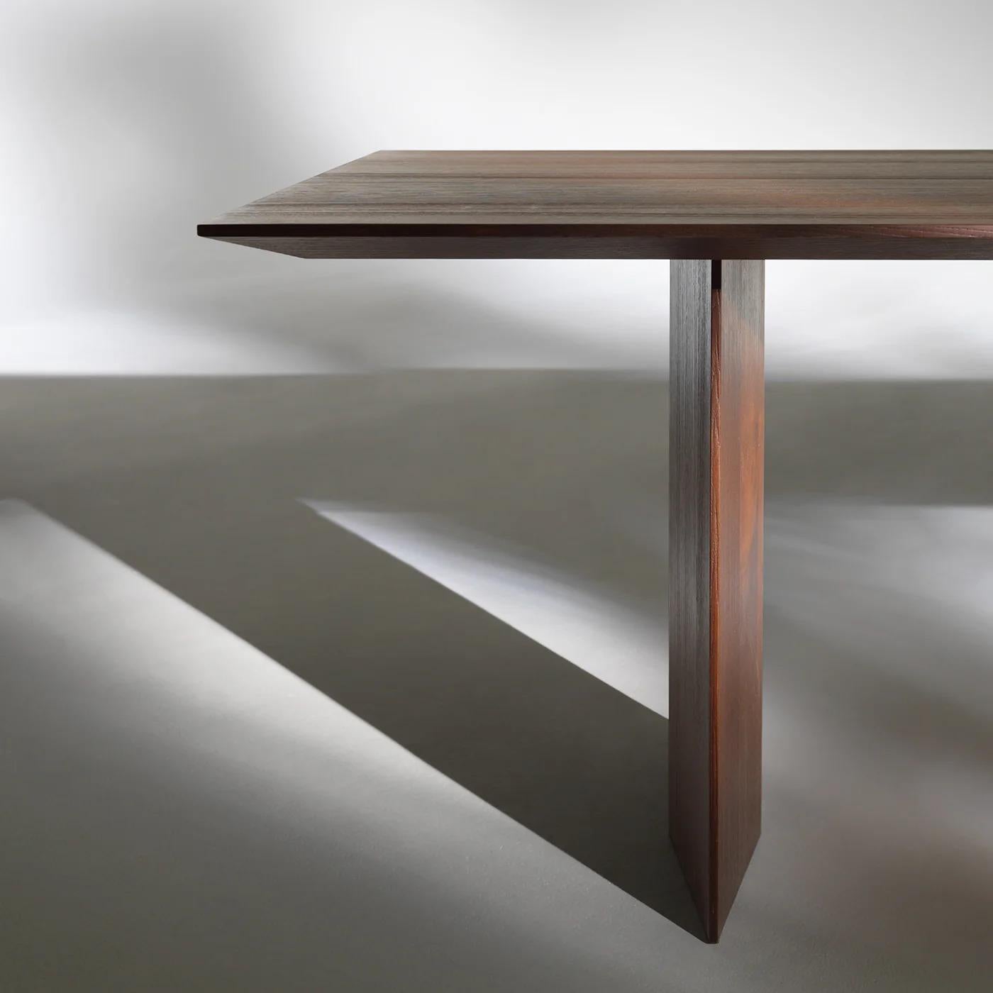 Fine dining table featuring a tabletop crafted from thermally treated ash veneer multilayer. Its minimalist design is defined by clean lines and a refined silhouette, supported by two sturdy rectangular legs positioned near the ends for optimal