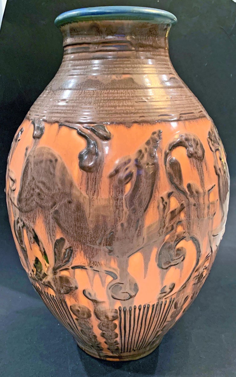 Richly glazed in tones of rosy pumpkin and blackish-brown, this large Art Deco vase is decorated with highly stylized depictions of prancing deer, surrounded by curling foliate motifs. The dark glaze of the figures drips down the face of the vase,