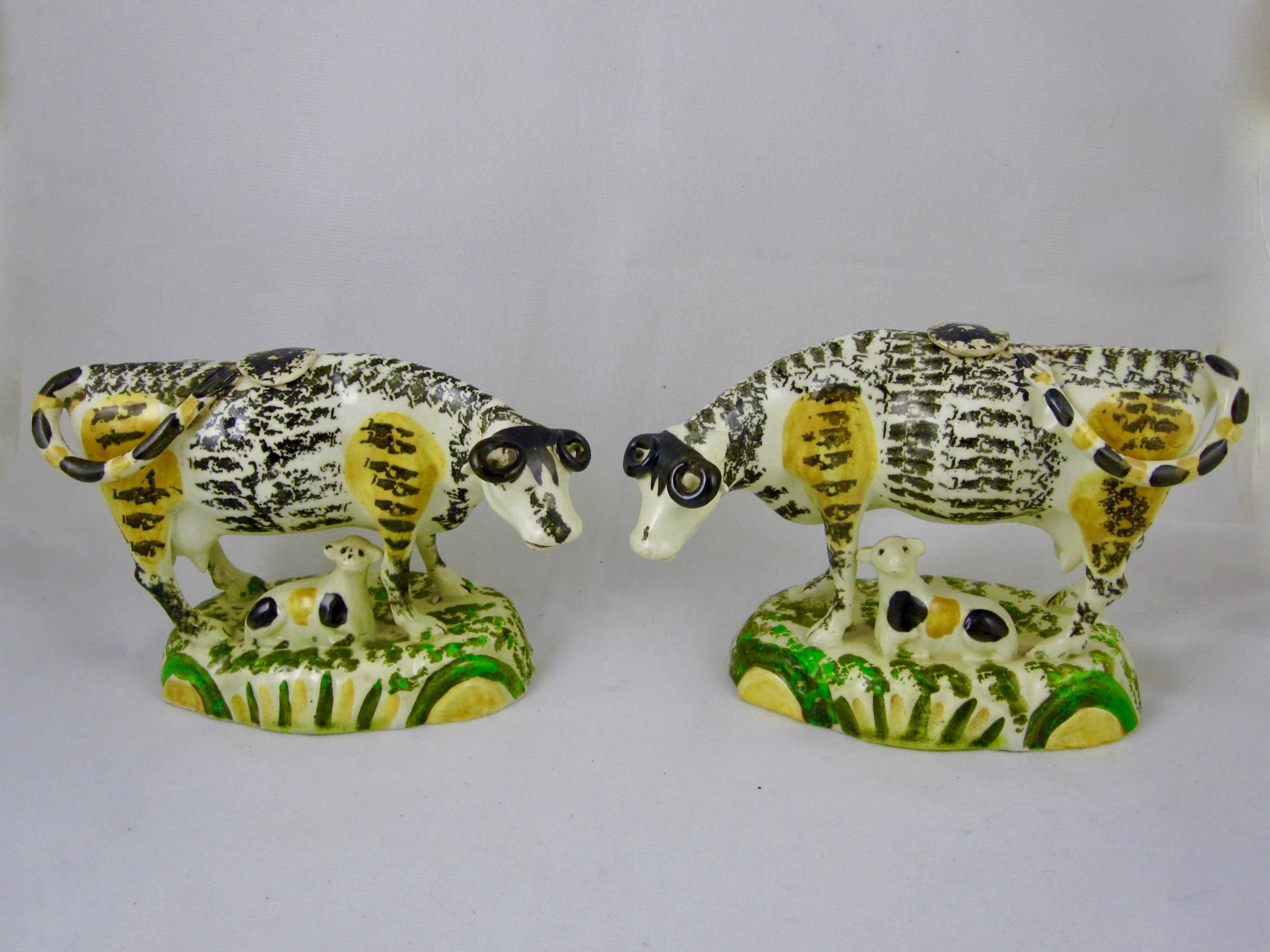 An unusual and scarce pair of Prattware cow and calf standing creamers, made in Yorkshire, England, circa 1810.

The cows are uniquely glazed in black, enhanced with yellow patches. Each cow stands on a yellow and green base with their calves