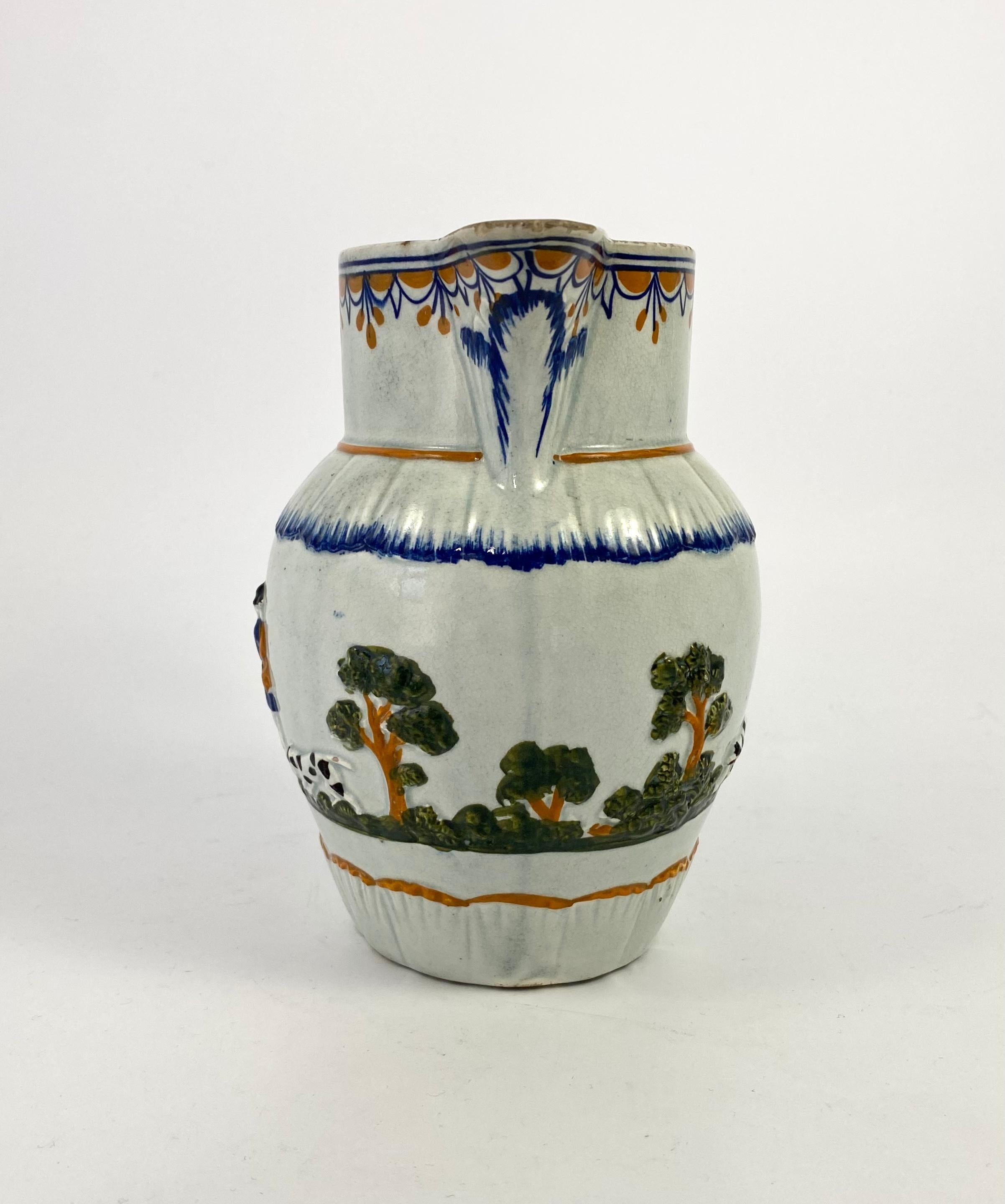 Prattware pottery Hunting jug, c. 1810. The finely potted jug, moulded with a continuous scene of huntsman, with spotted hounds, walking amongst trees, coloured in Pratt glazes. Having a dolphin moulded handle, and acanthus moulded spout, with a