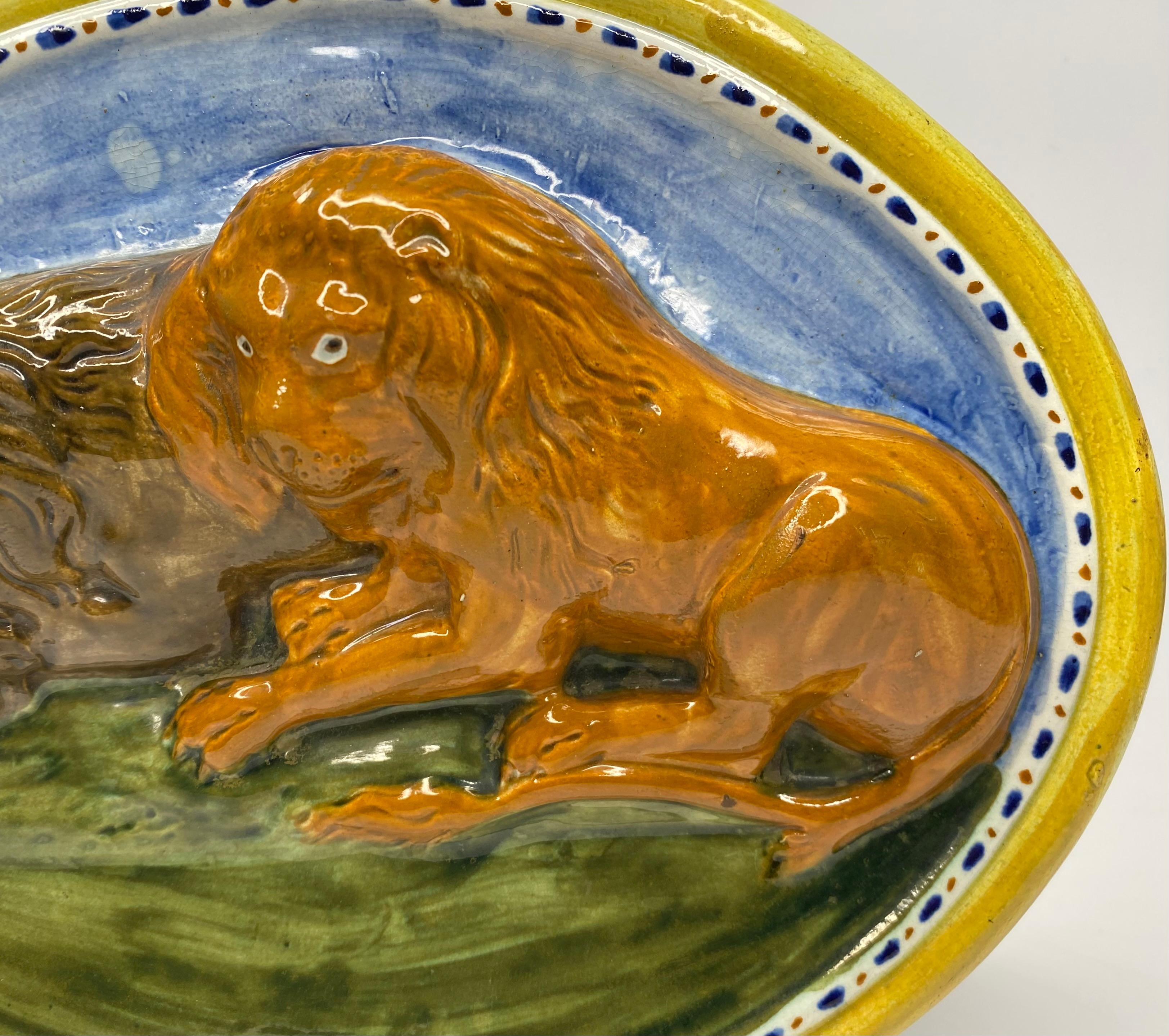 Staffordshire pottery Prattware Lions plaque, c. 1810. The large, oval plaque moulded in deep relief, with two male lions, laid on grass, beneath blue sky. Decorated in vibrant Pratt style glaze, one lion in brown, the other in ochre. Within a thin